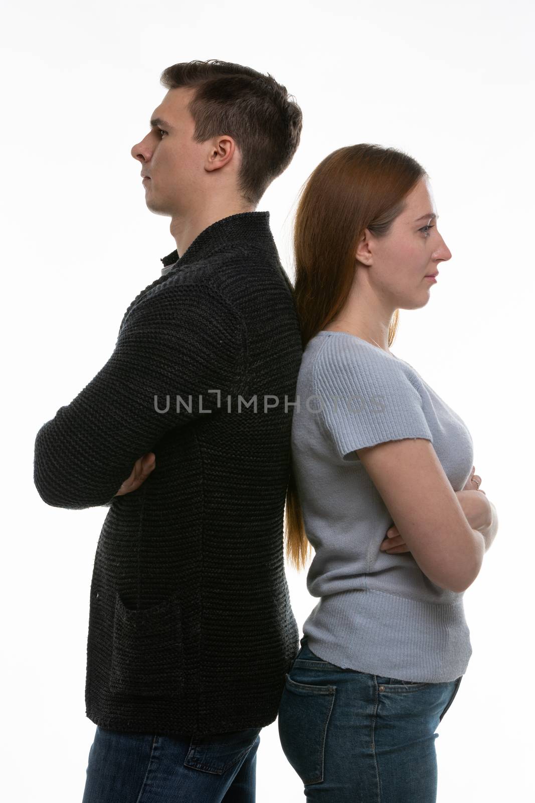A man and a woman stand with their backs to each other, with their arms folded on their chests