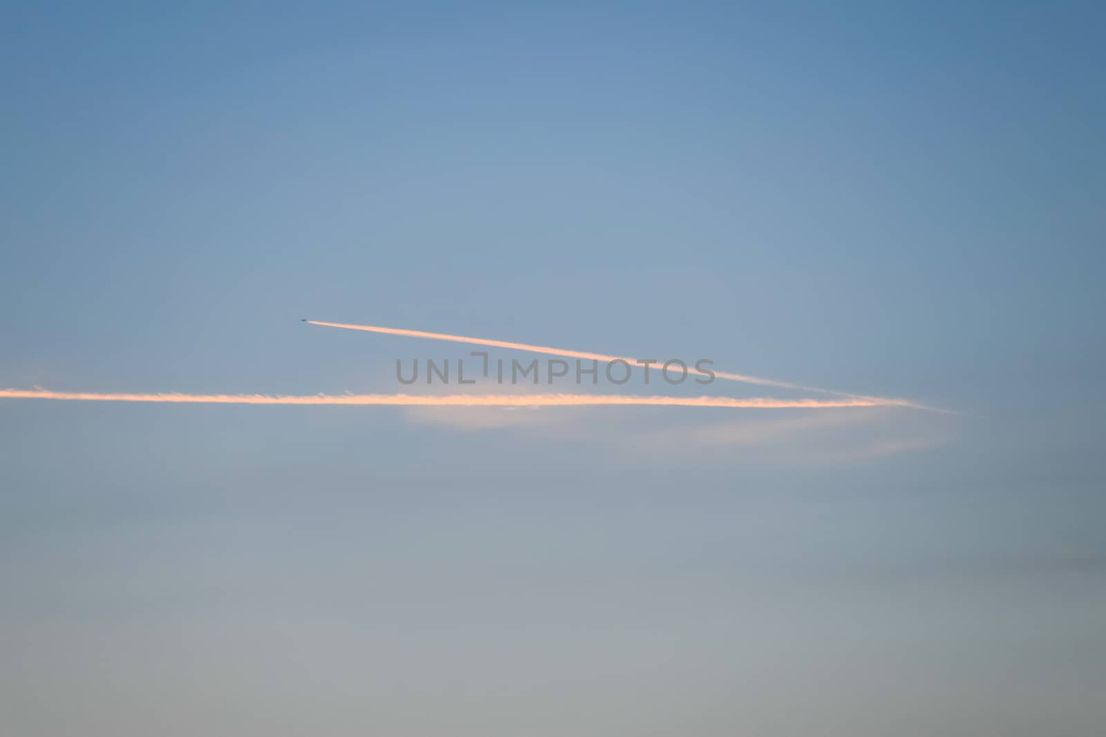 Contrail from airplane on a blue sky against a sunset. by fedoseevaolga