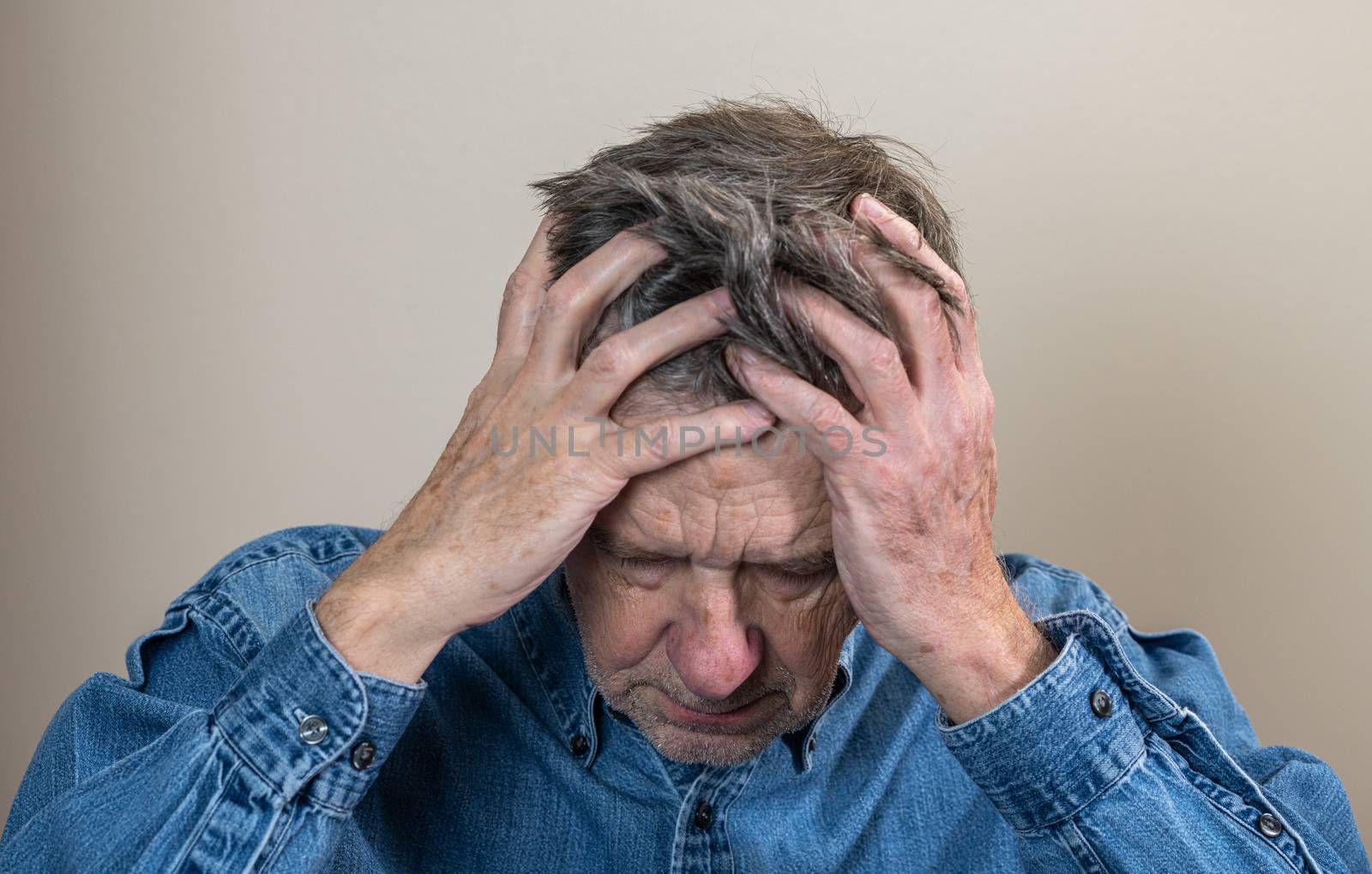 Head and shoulders portrait of a senior caucasian man with head in hands and looking depressed