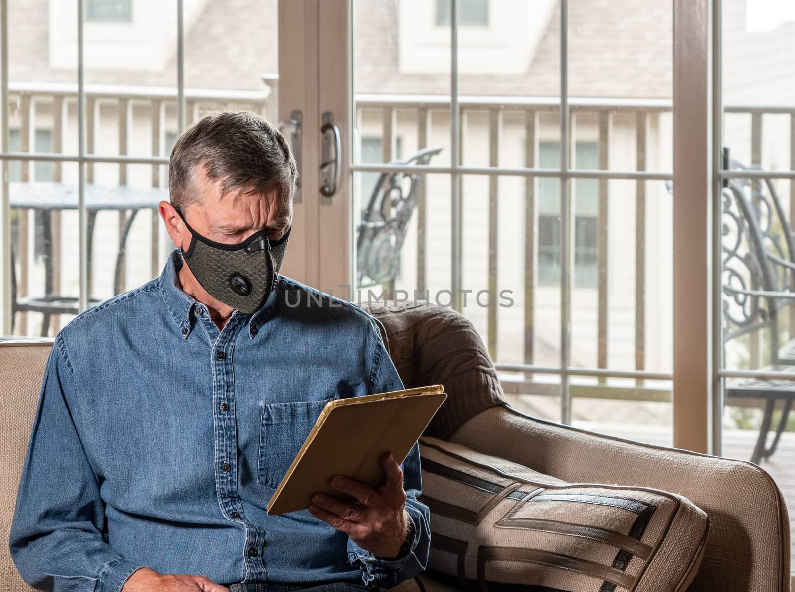 Concerned and worried man wearing a protective breathing mask against flu and coronavirus and reading news on tablet