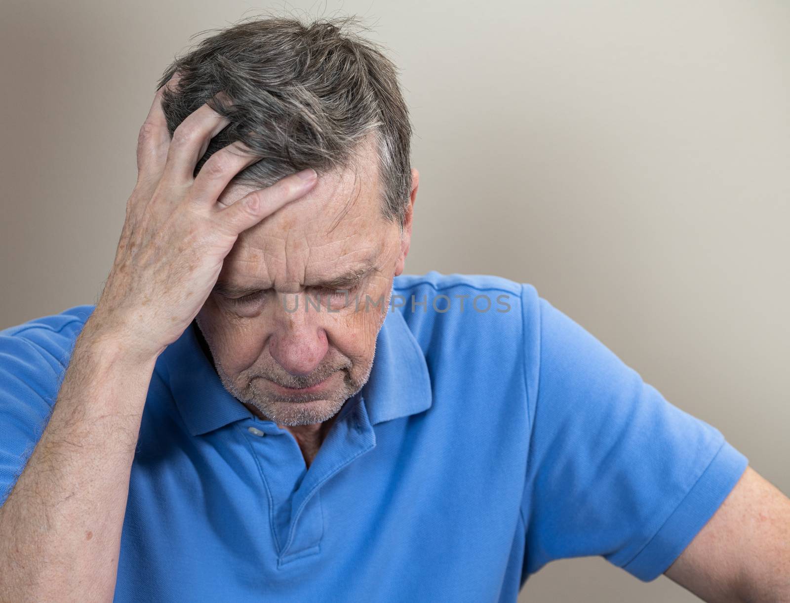 Head and shoulders portrait of a senior caucasian man with head in hands and looking depressed