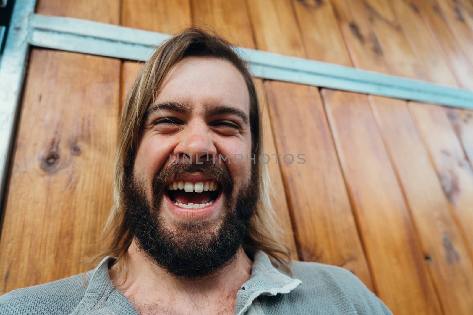 Young man with a beard laughing on a wooden background