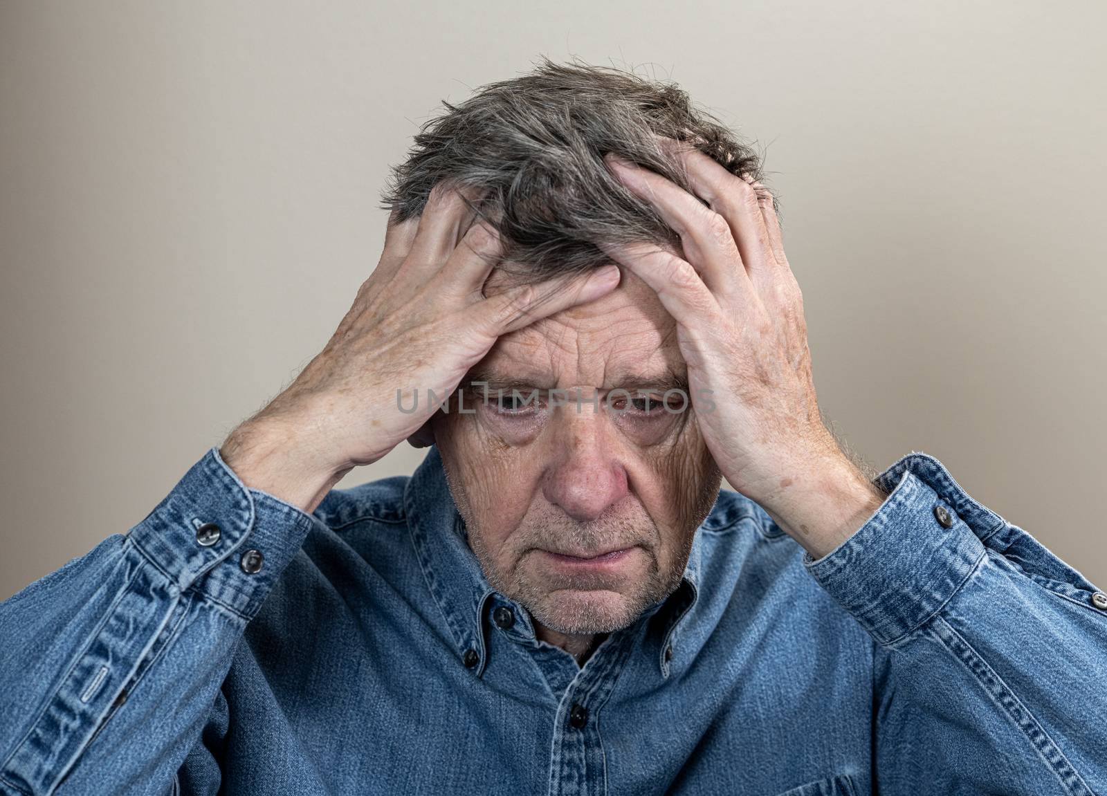 Head and shoulders portrait of a senior caucasian man with head in hands and looking depressed
