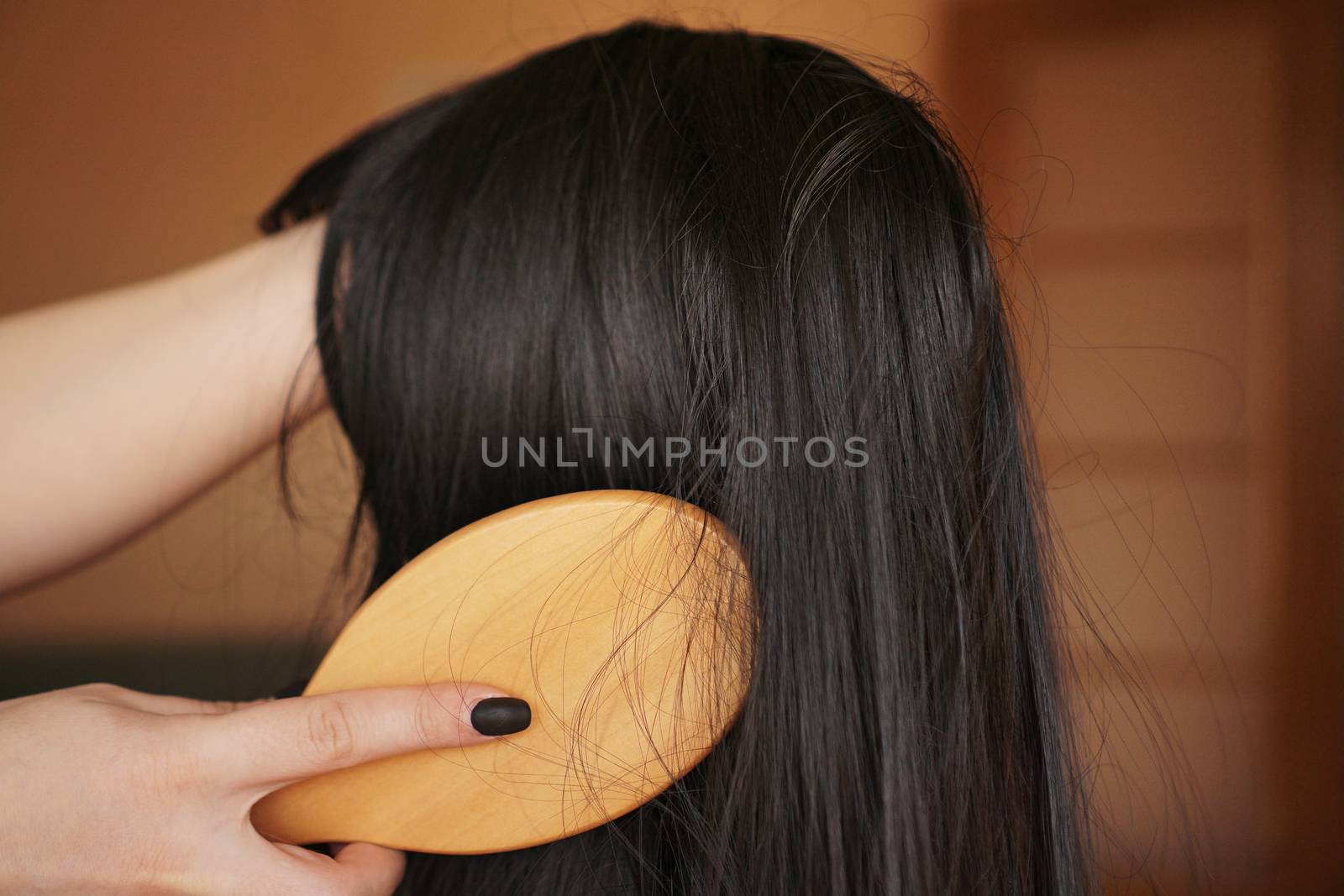 Female hand holds a black wig with long hair and combs a wooden comb by natali_brill