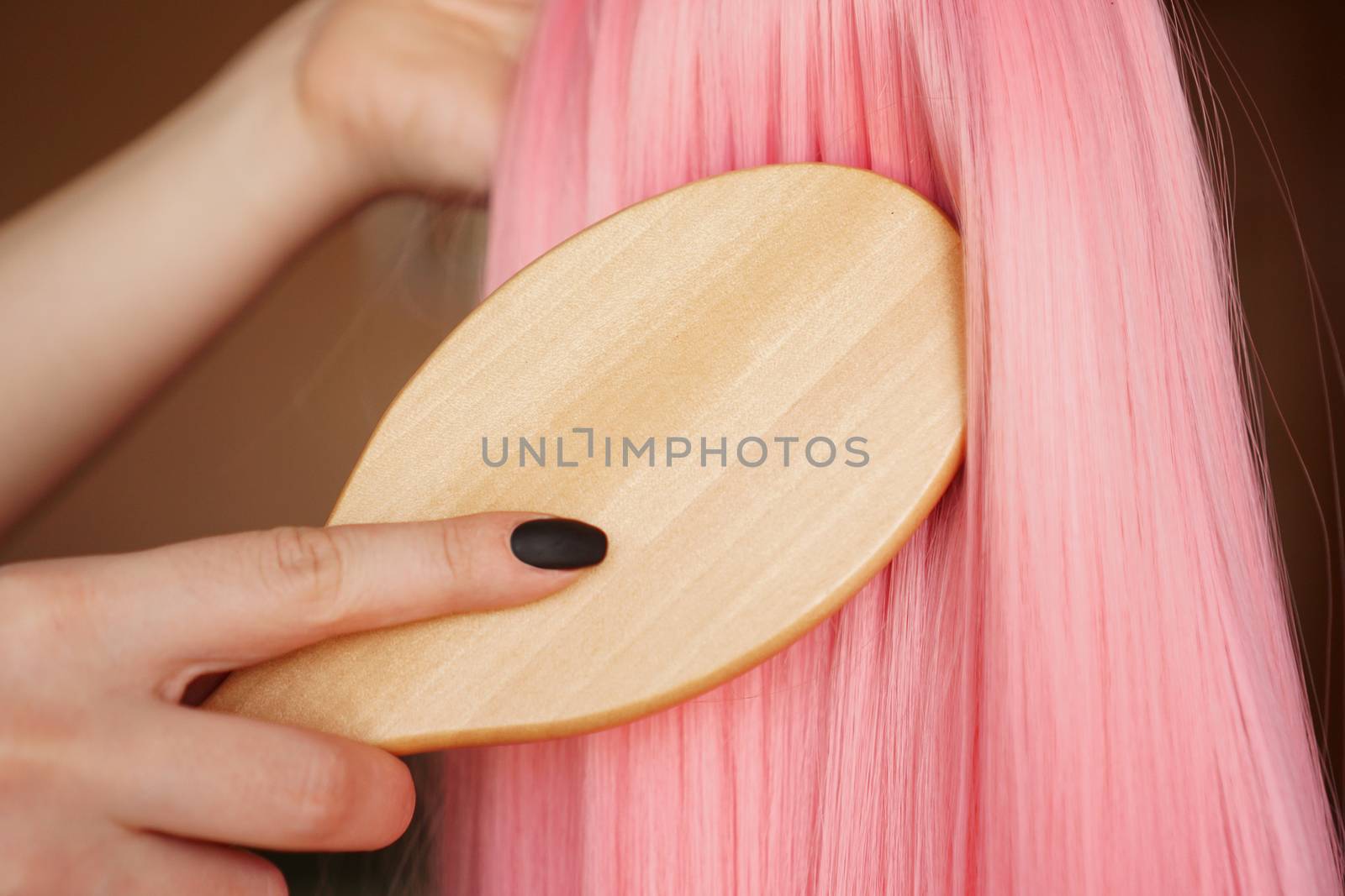 Female hand holds a pink wig with long hair and combs a wooden comb. Hairdresser and hair care