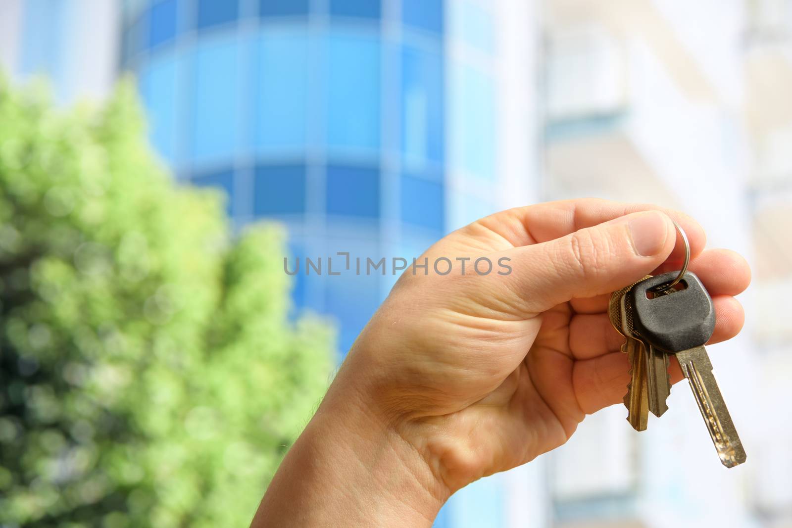 The customer holds the keys to the new apartment against the background of a modern glass building on a sunny day