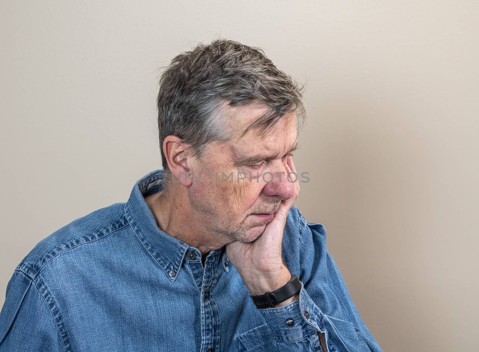 Head and shoulders portrait of a senior caucasian man with head in hands and looking depressed