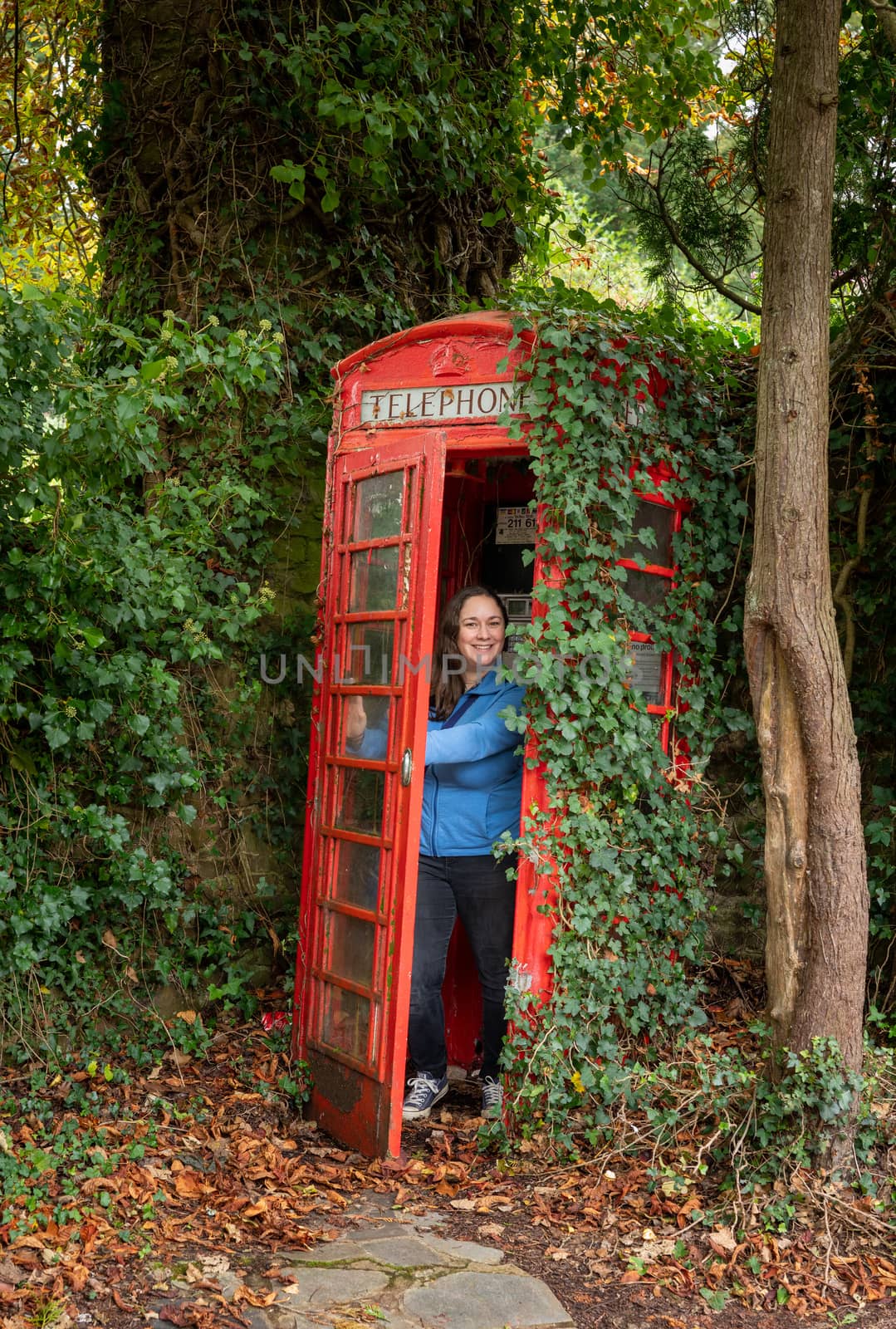 Classic red phonebox in English countryside with woman coming out by steheap