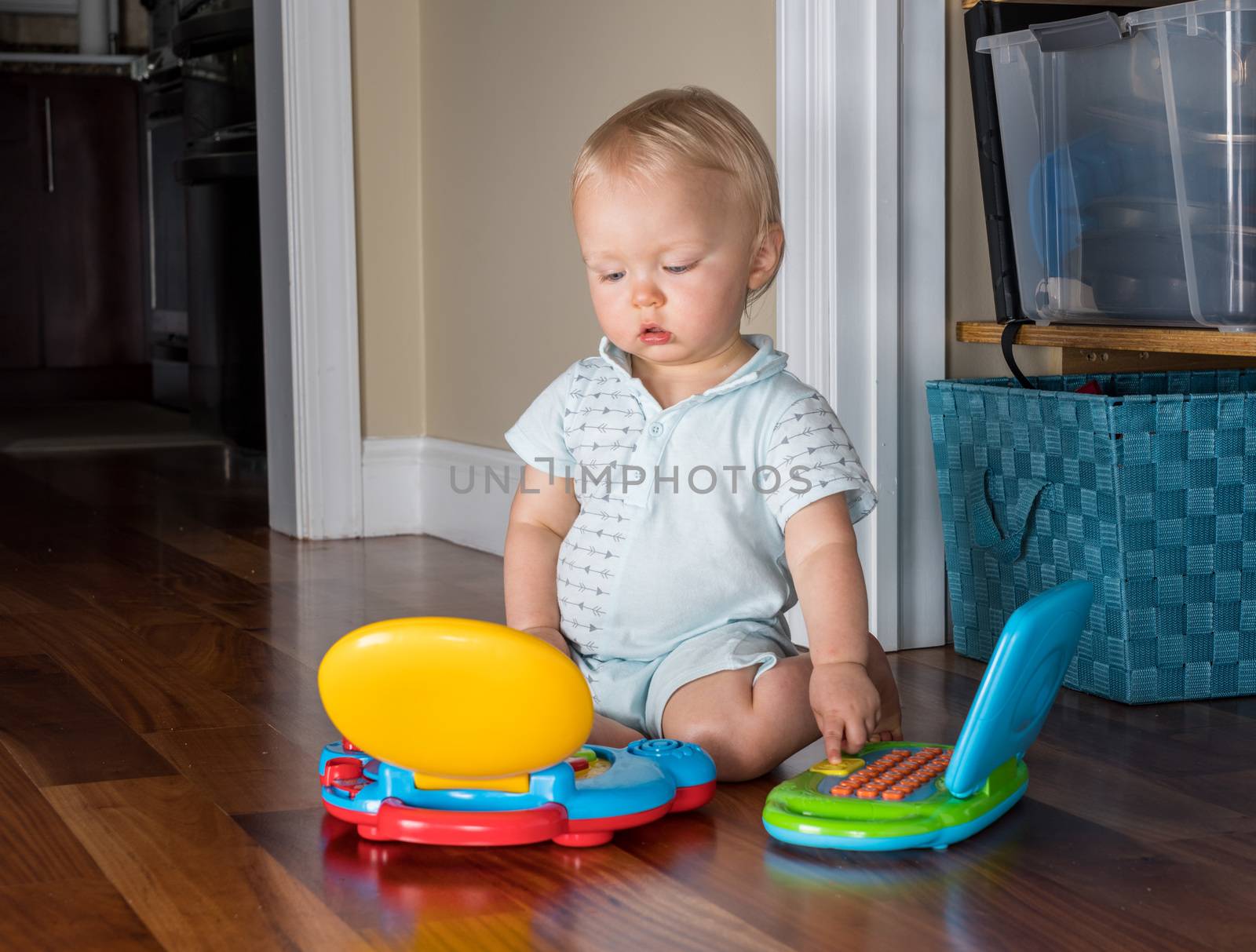 Baby boy sitting on the wooden floor of living room and playing with two toy computers at the same time