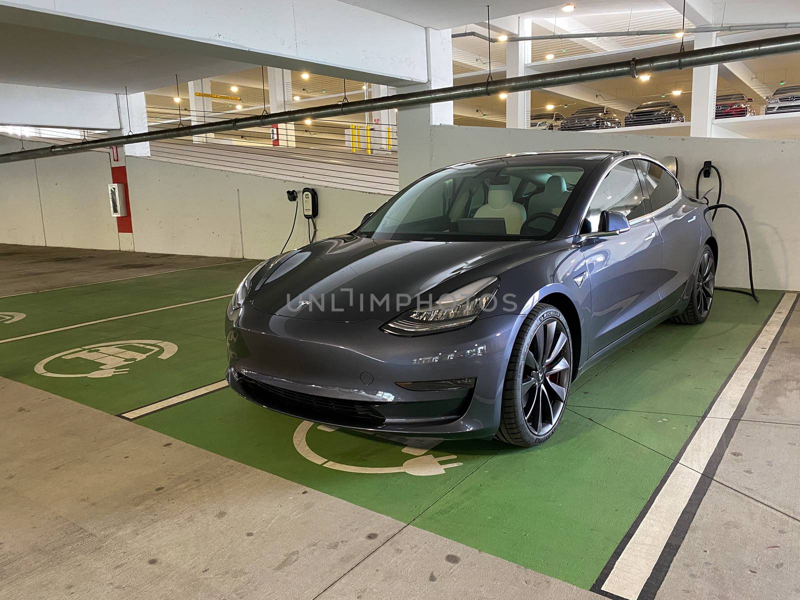 A gray Tesla Model 3 charging at a free garage charging station. by Jshanebutt