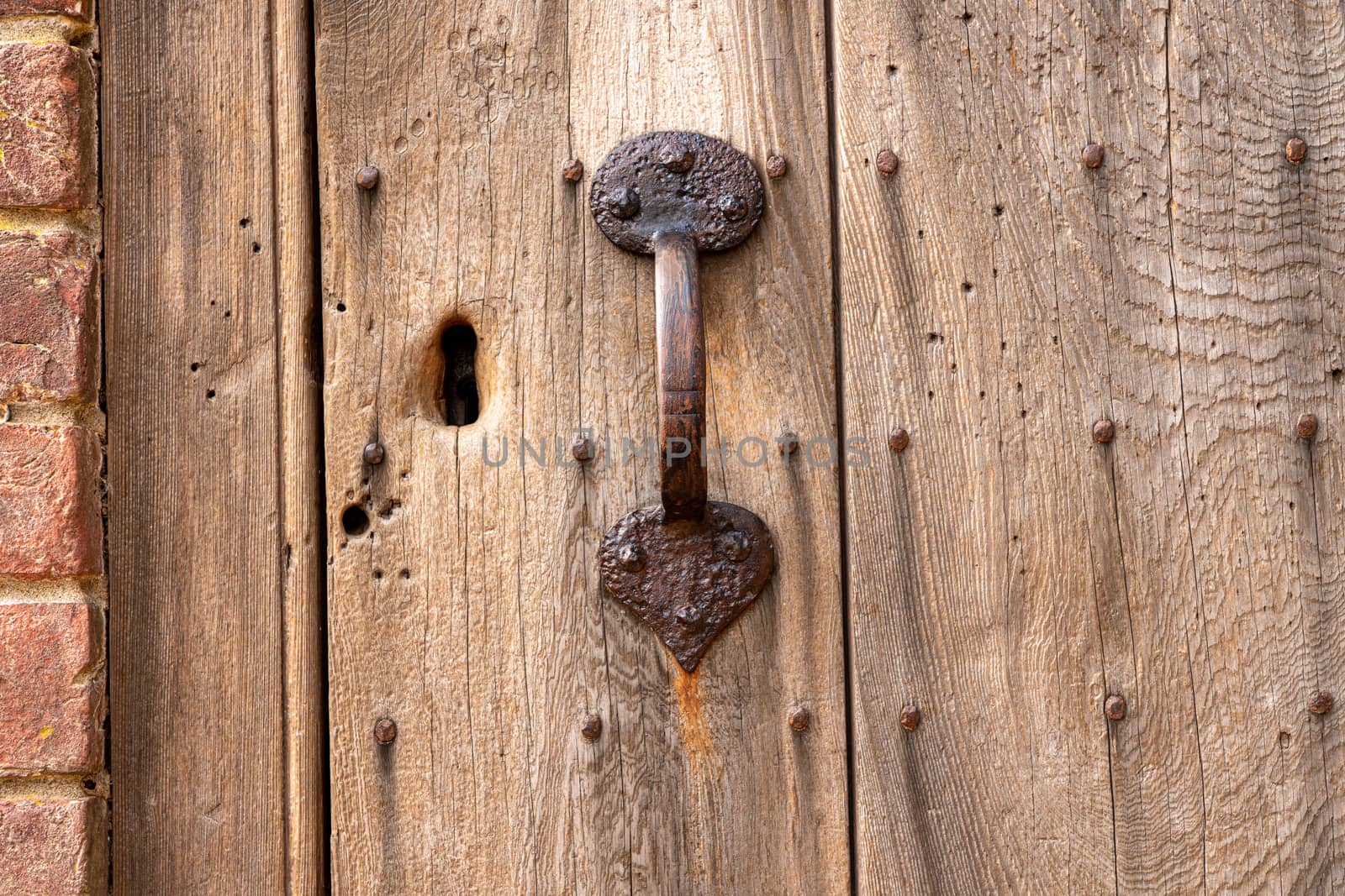 Ancient exterior door in worn and weathered wood with rusty handle and key hole for lock