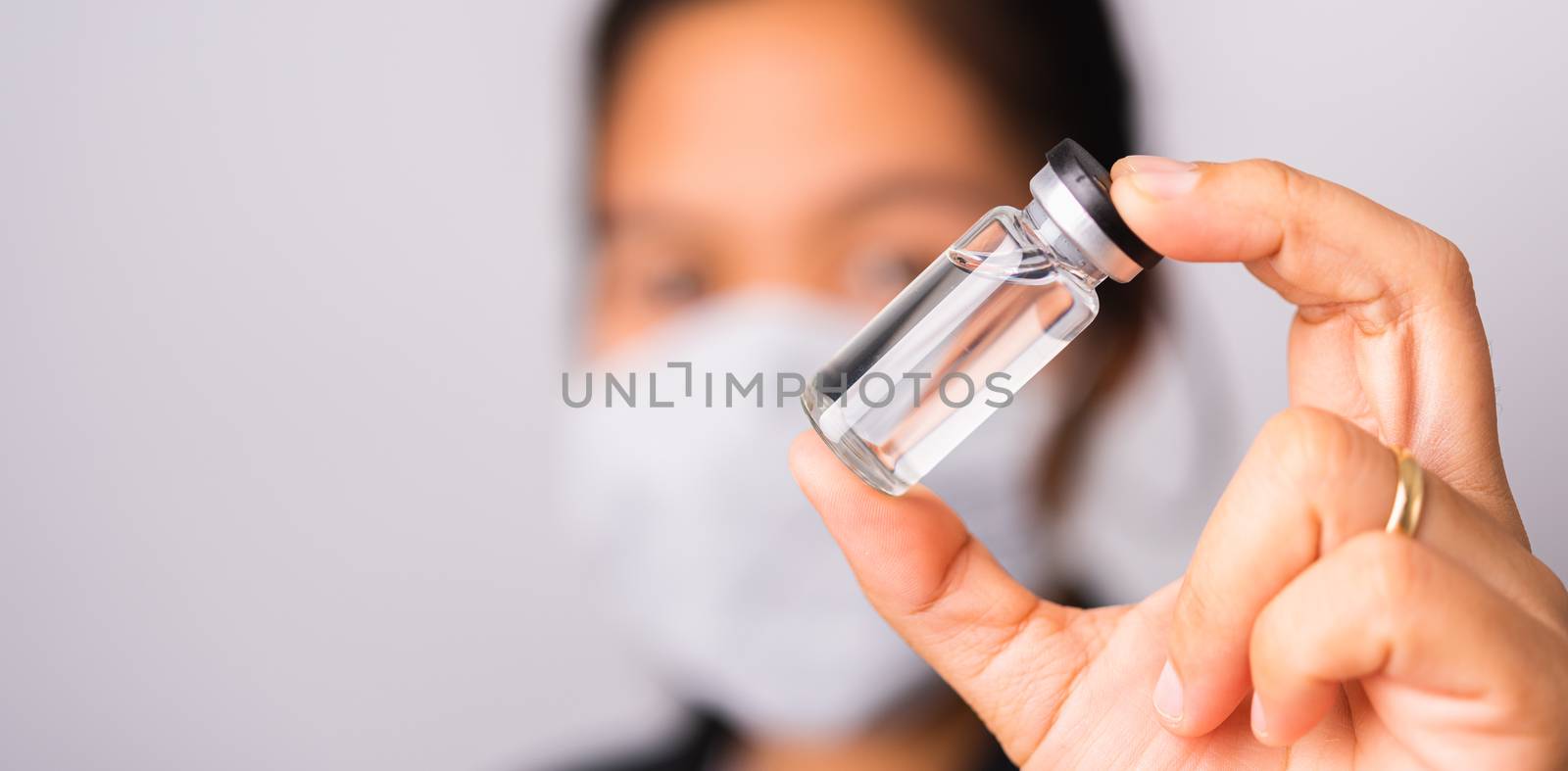 Asian woman doctor wearing surgical protective cloth face mask against coronavirus her hold ampoule bottle vaccine focus on  glass transparent, studio shot isolated white background, COVID-19 concept