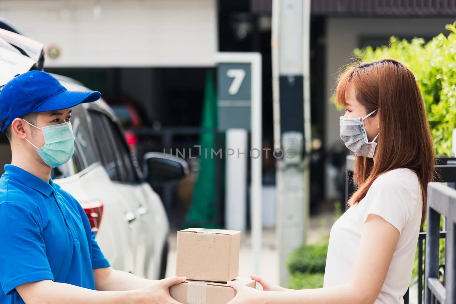 Asian young delivery man courier shopping online give package post box he protective face mask service woman customer receiving box at front home, under curfew quarantine pandemic coronavirus COVID-19