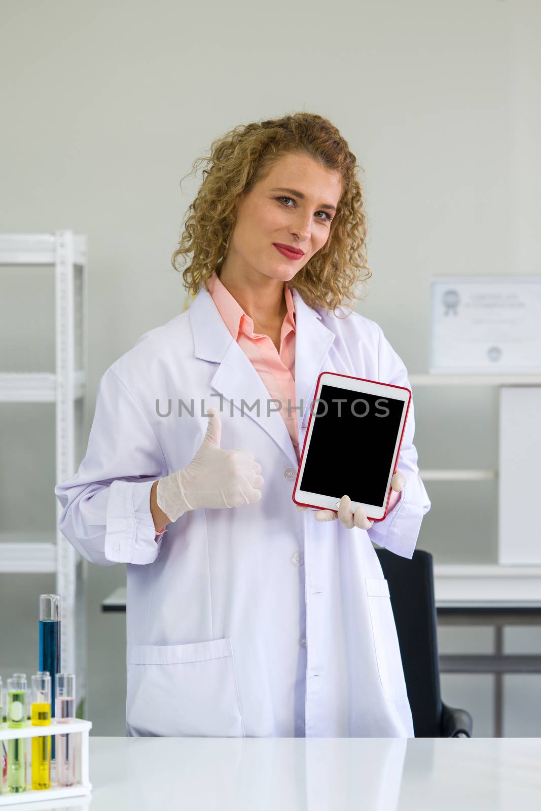 A young blonde scientist holding blank screen tablet computer. Working atmosphere in chemical laboratory.