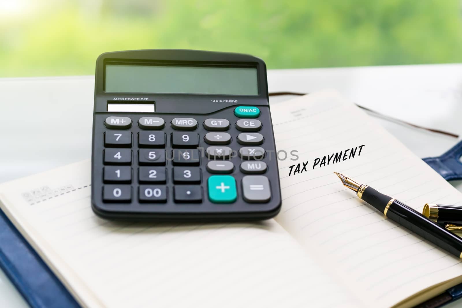 pen, calculator and notebook with TAX PAYMENT word on the white table with green backgrounds