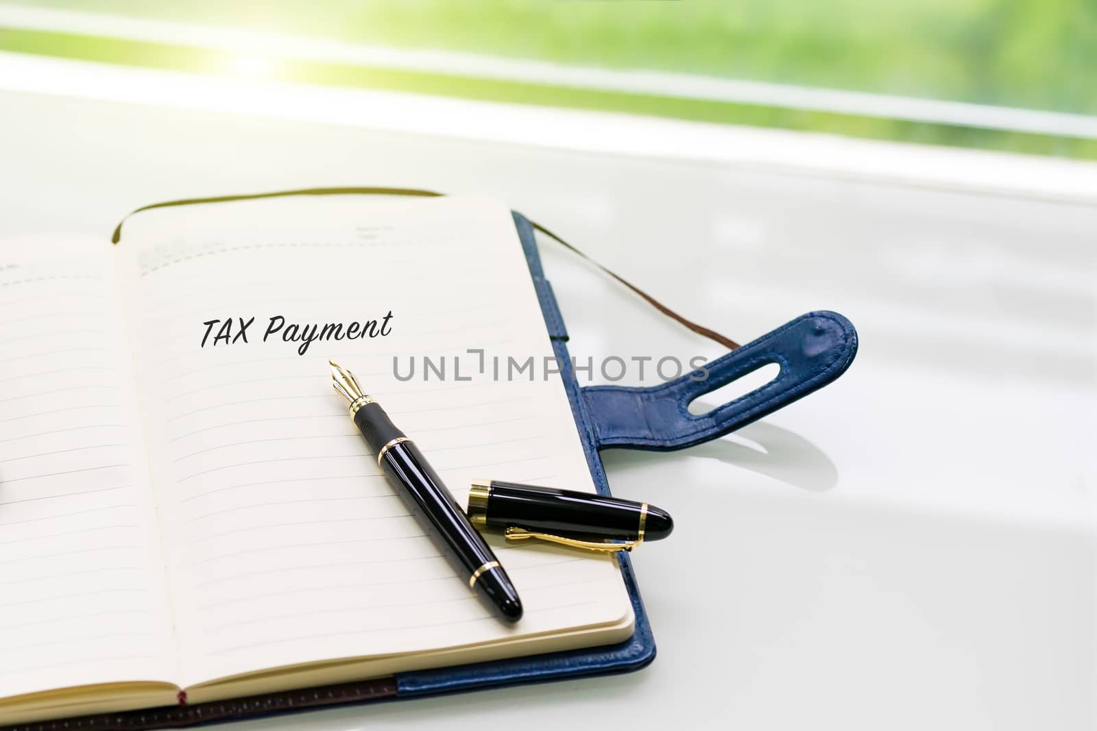 pen and notebook with TAX Payment word on the white table near window, sideview with green light backgrounds