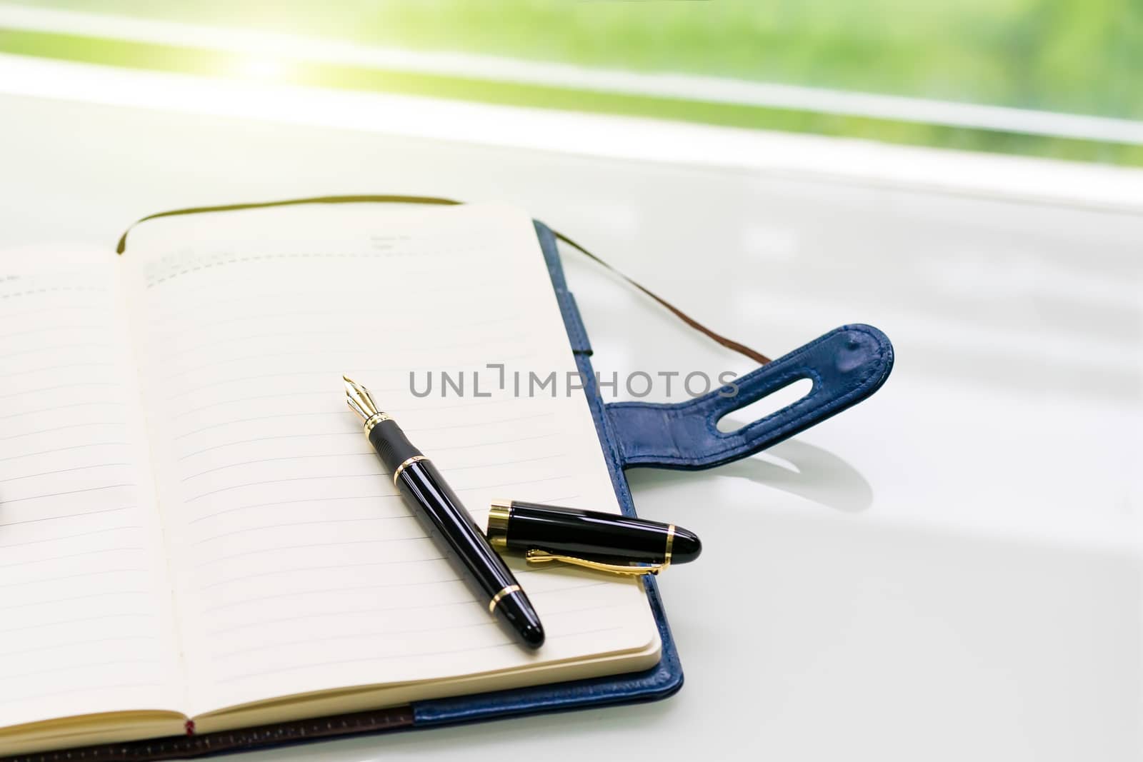 pen and notebook on the white table near window, sideview with green light backgrounds
