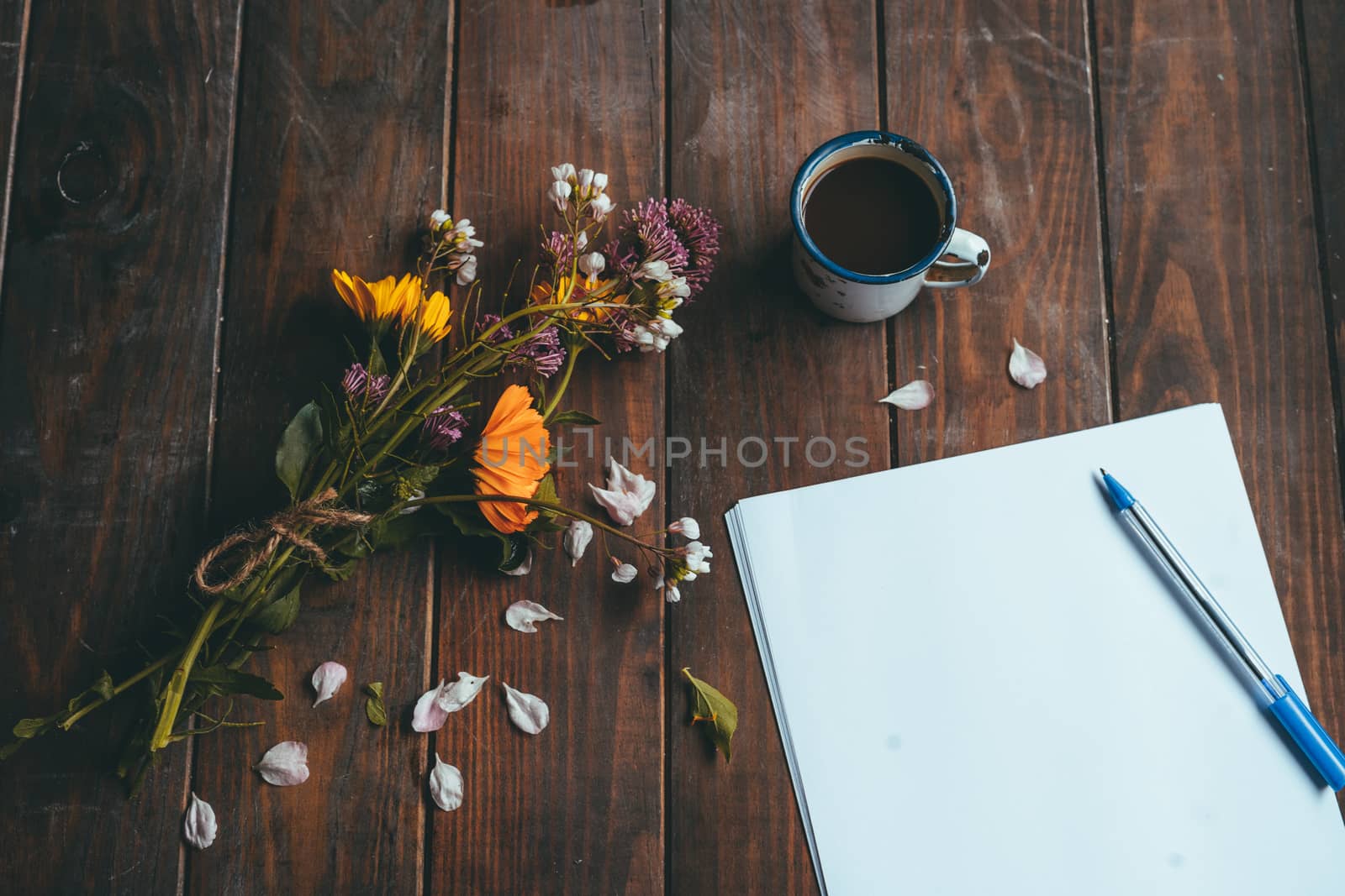 Blank paper and pen with spring flowers with a small white cup of coffee on a rustic wooden table