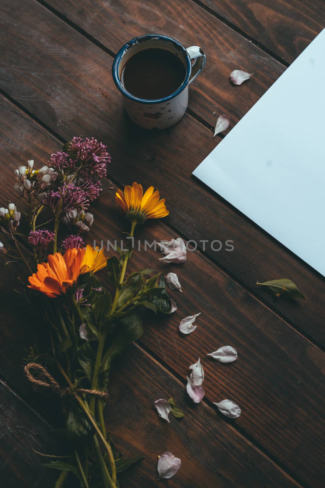 Blank paper with spring flowers with a small white cup of coffee on a rustic wooden table