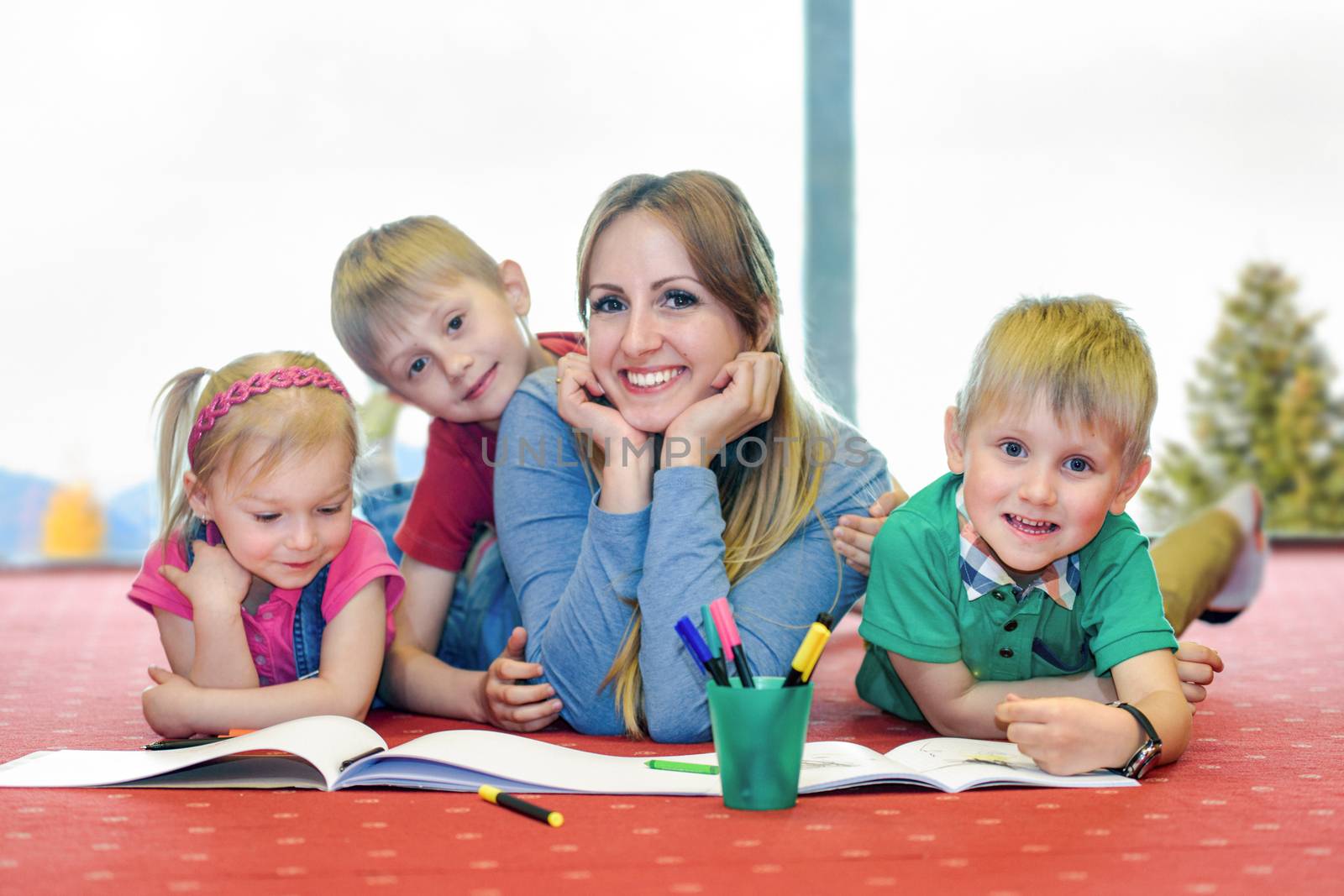 Happy mother with her children lies on the carpet in the apartment and plays with coloring the pictures