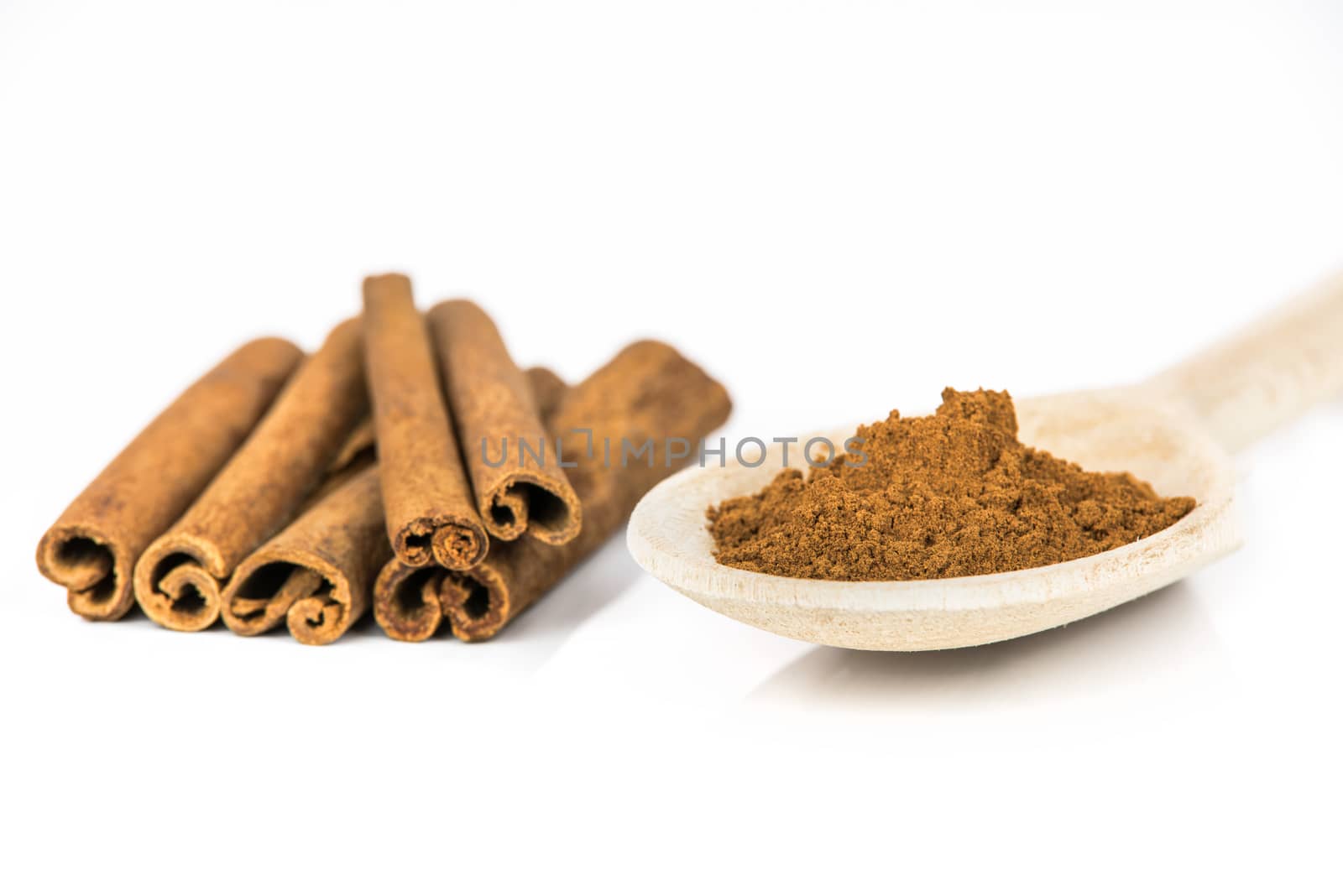 Cinnamon sticks and wooden spoon with ground cinnamon powder on white background