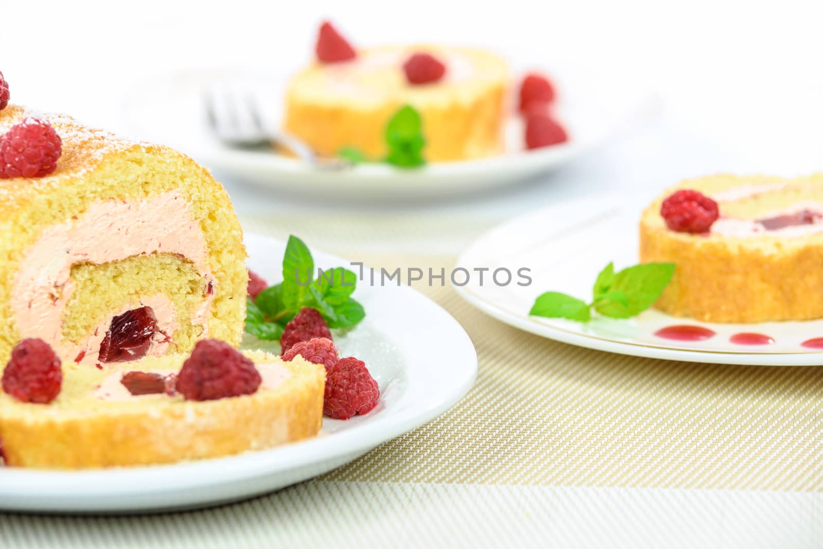 Delicious homemade roll cake with raspberry filling sprinkled with powdered sugar and raspberries and mint