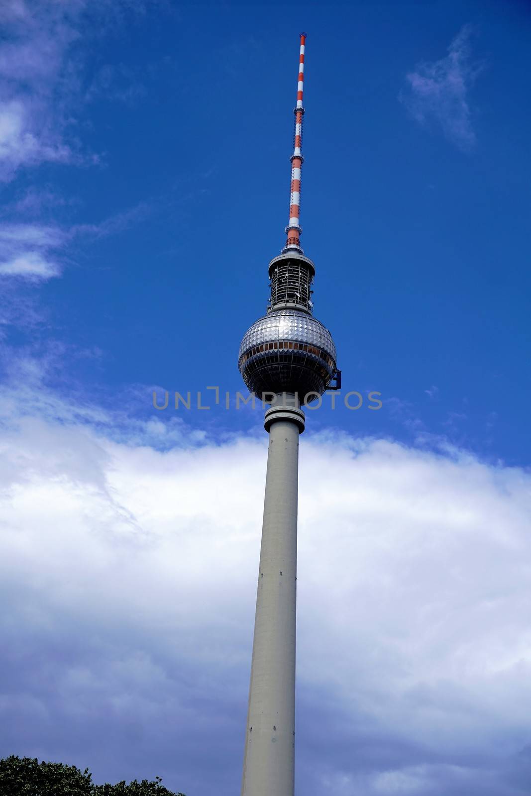 Berlin television tower in front of blue sky with clouds and trees