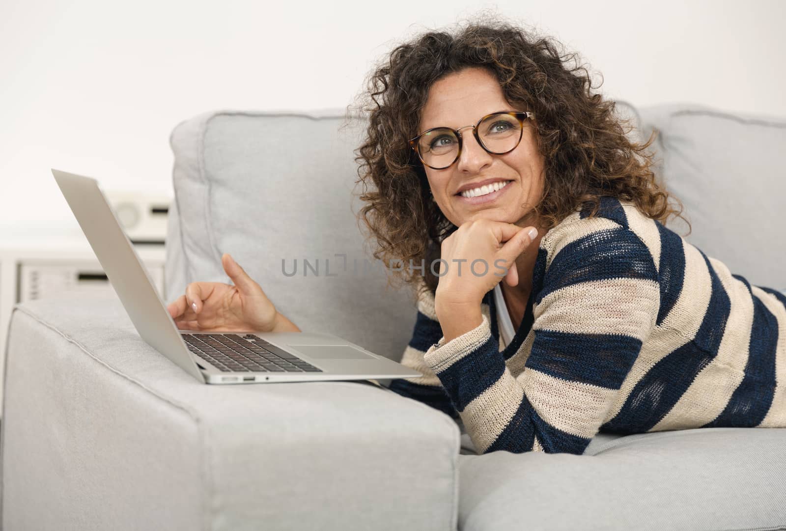 Beautiful woman at home lying on the sofa and working with a laptop