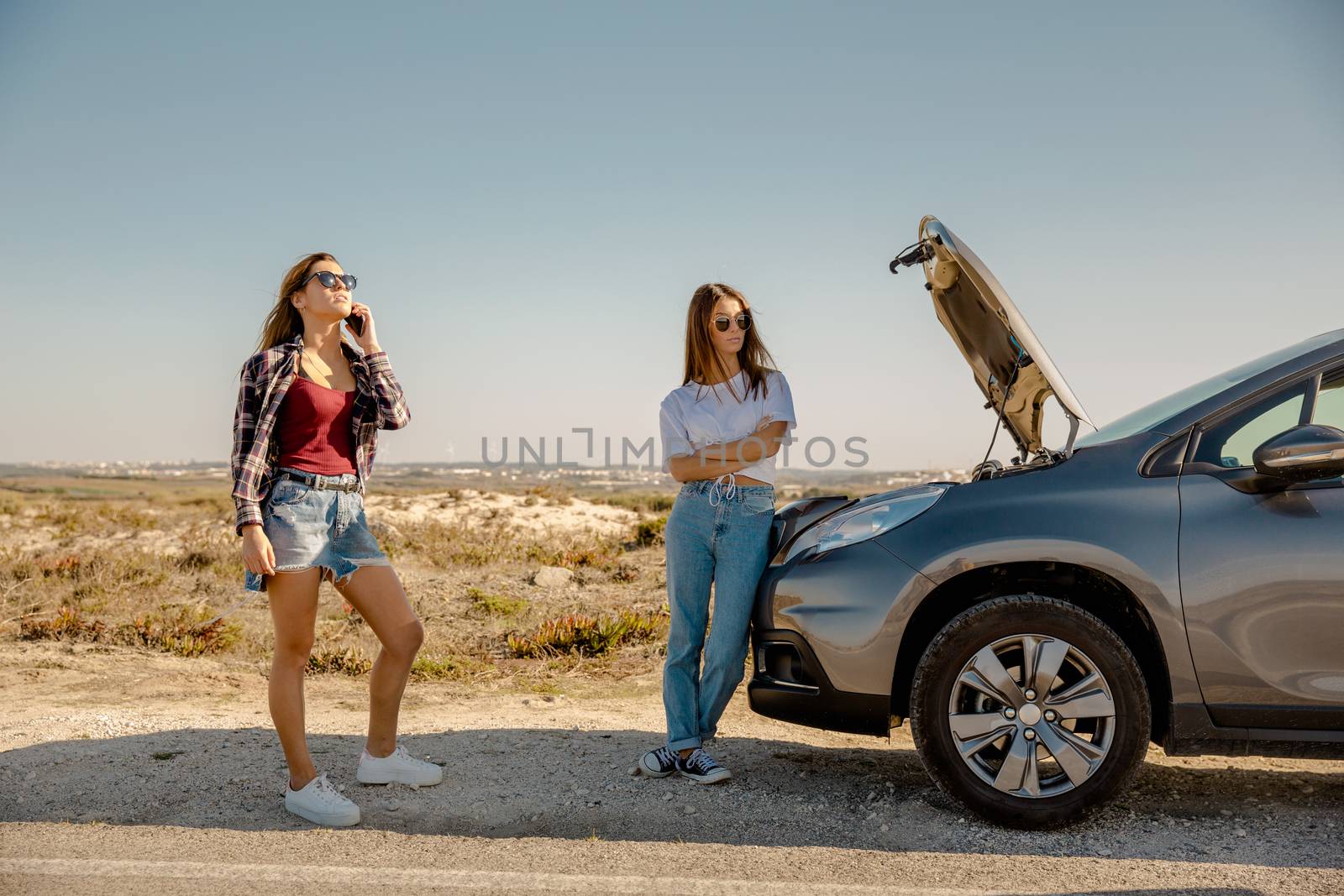 Female friends examining broken down car on country road 