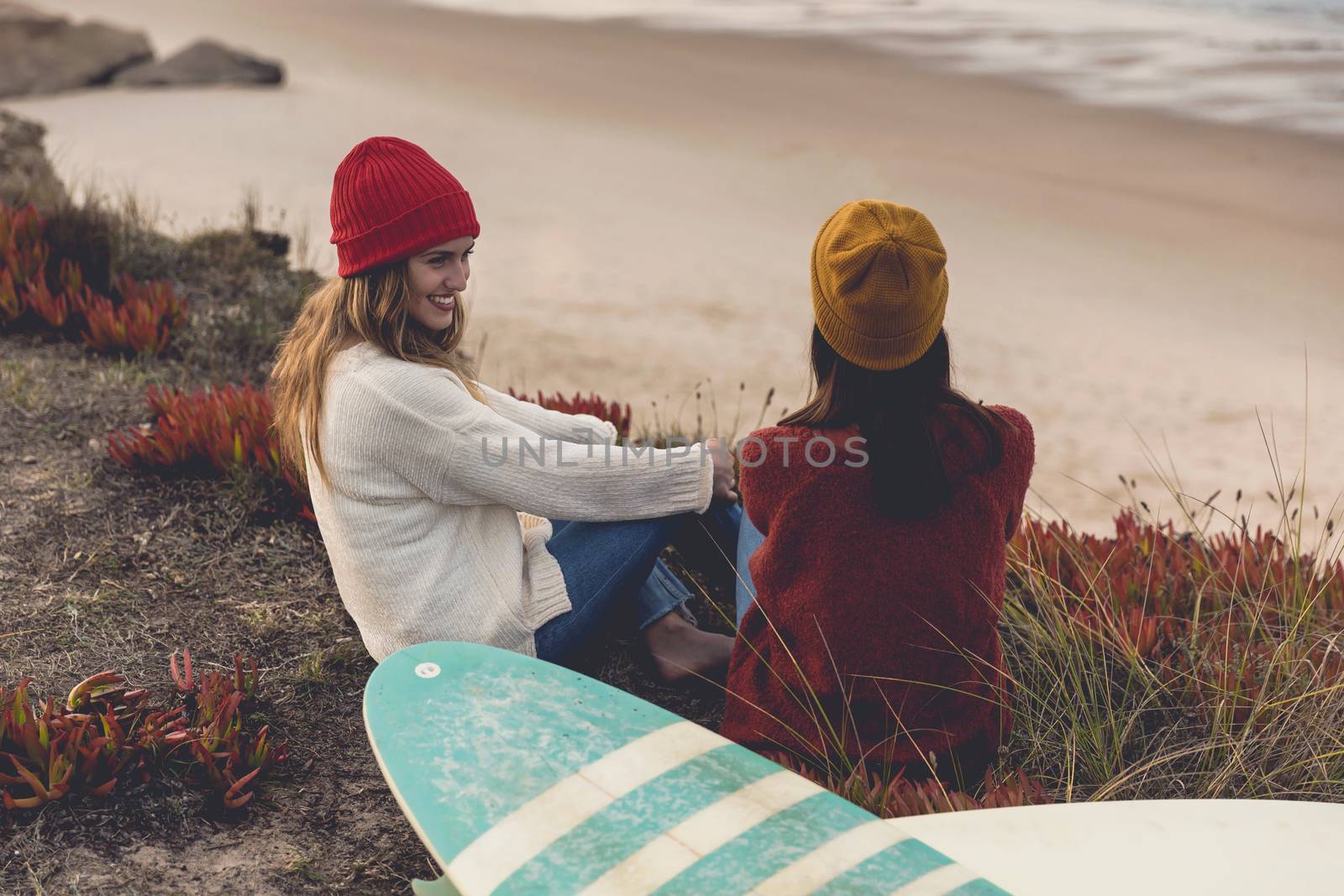 Two best friends sitting near the coastline with her surfboards while looking to the ocean