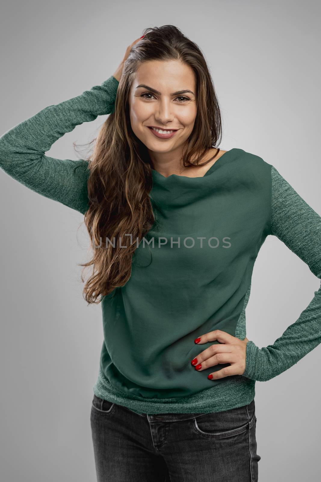 Beautiful woman standing over a gray background with her hand on the hair and smiling