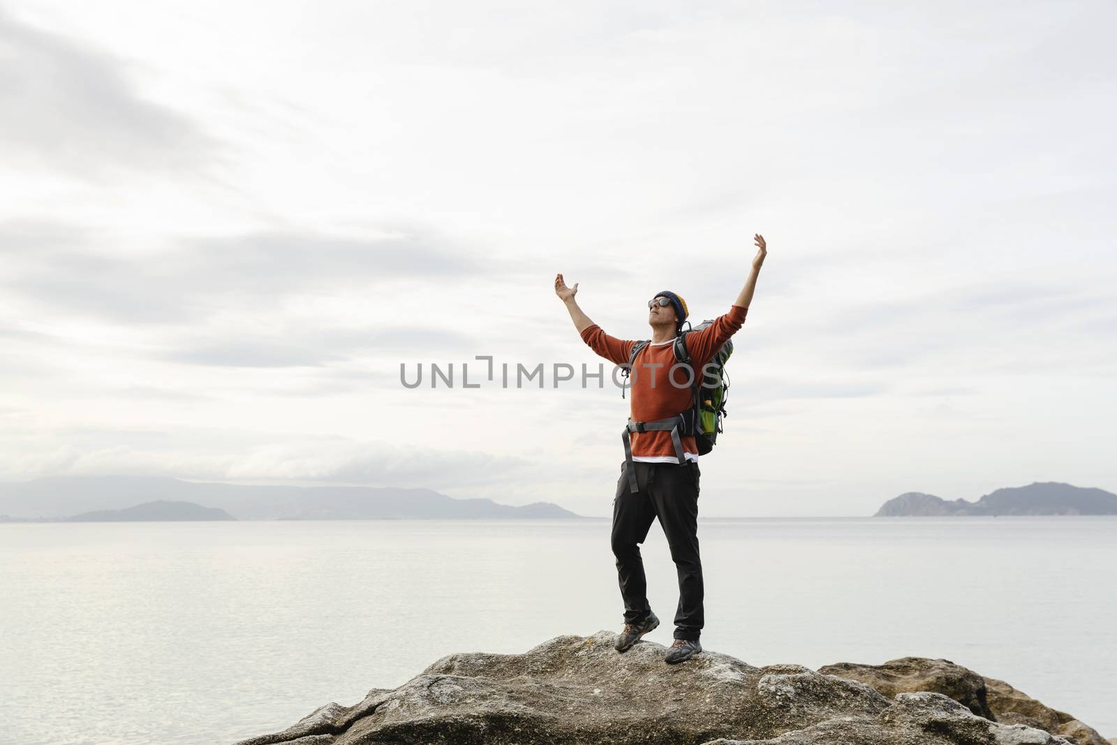 Man with backpack and arms raised  enjoying the beautiful morning view of the coast