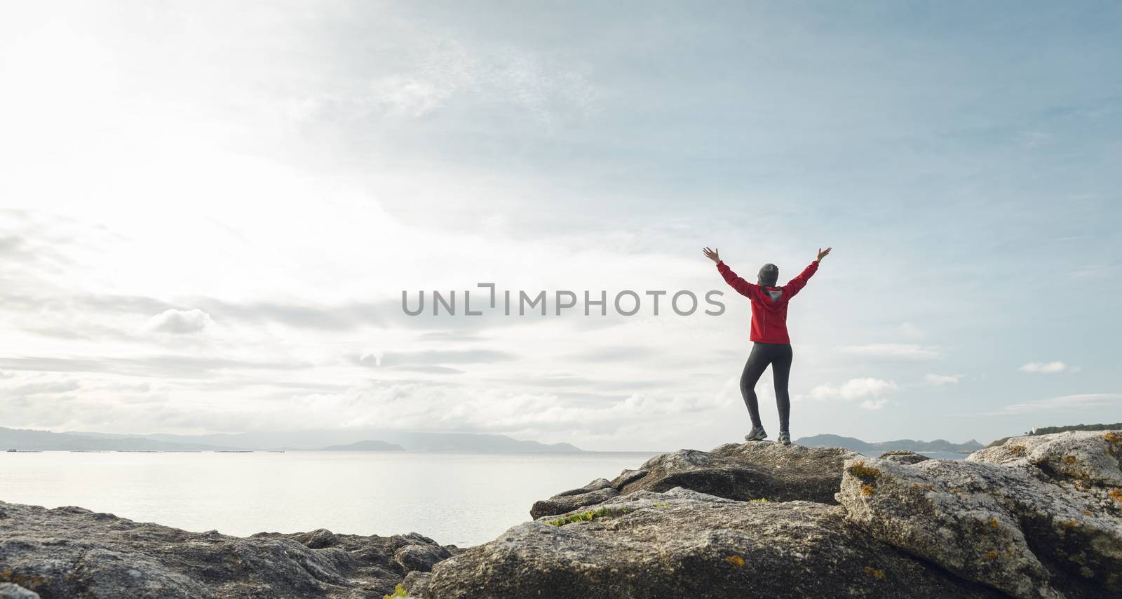 Woman with arms raised  enjoying the beautiful morning view of the coast