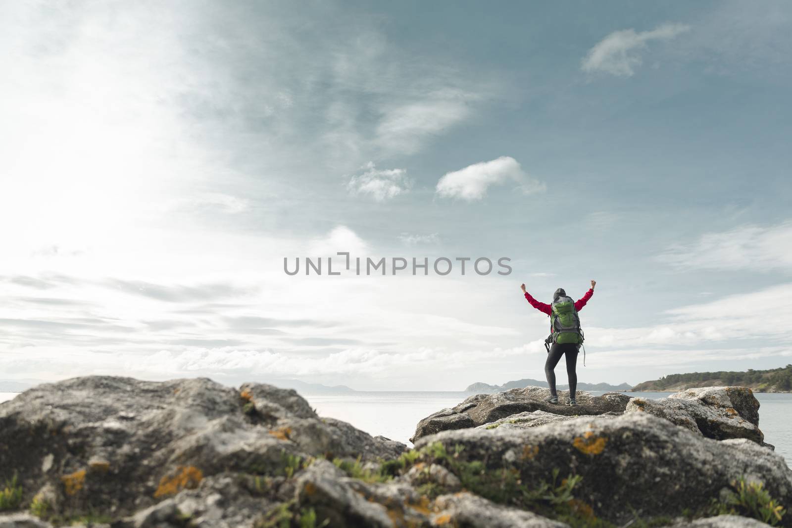 Woman with backpack and arms raised  enjoying the beautiful view of the coast