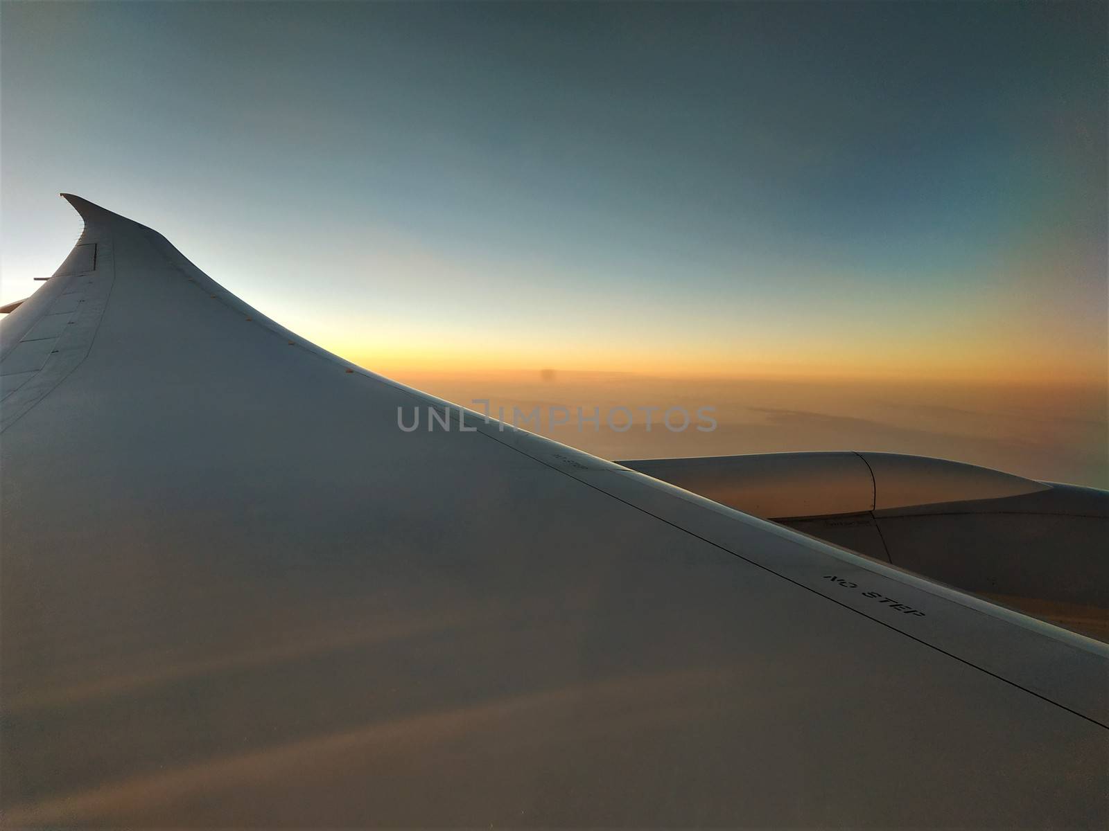 View out of plane window over a wing into the sunset