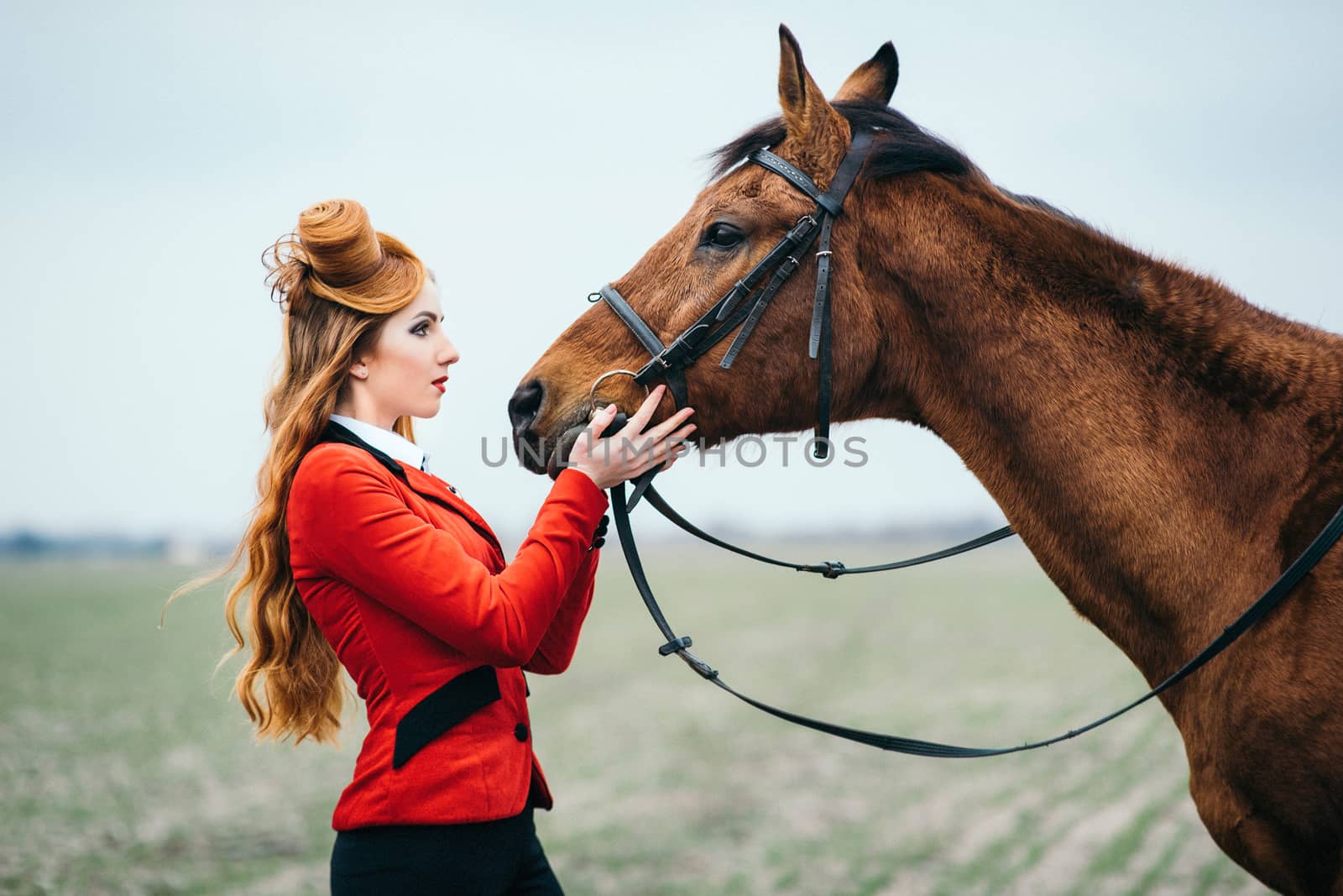 red-haired jockey girl in a red cardigan and black high boots with a horse for a walk