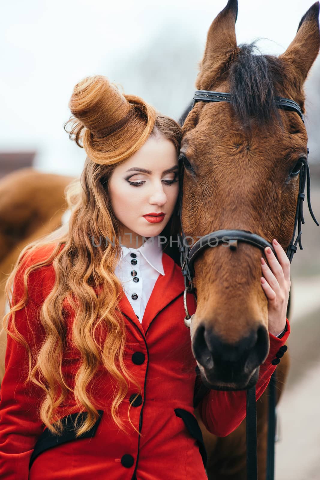 red-haired jockey girl in a red cardigan and black high boots with a horse for a walk