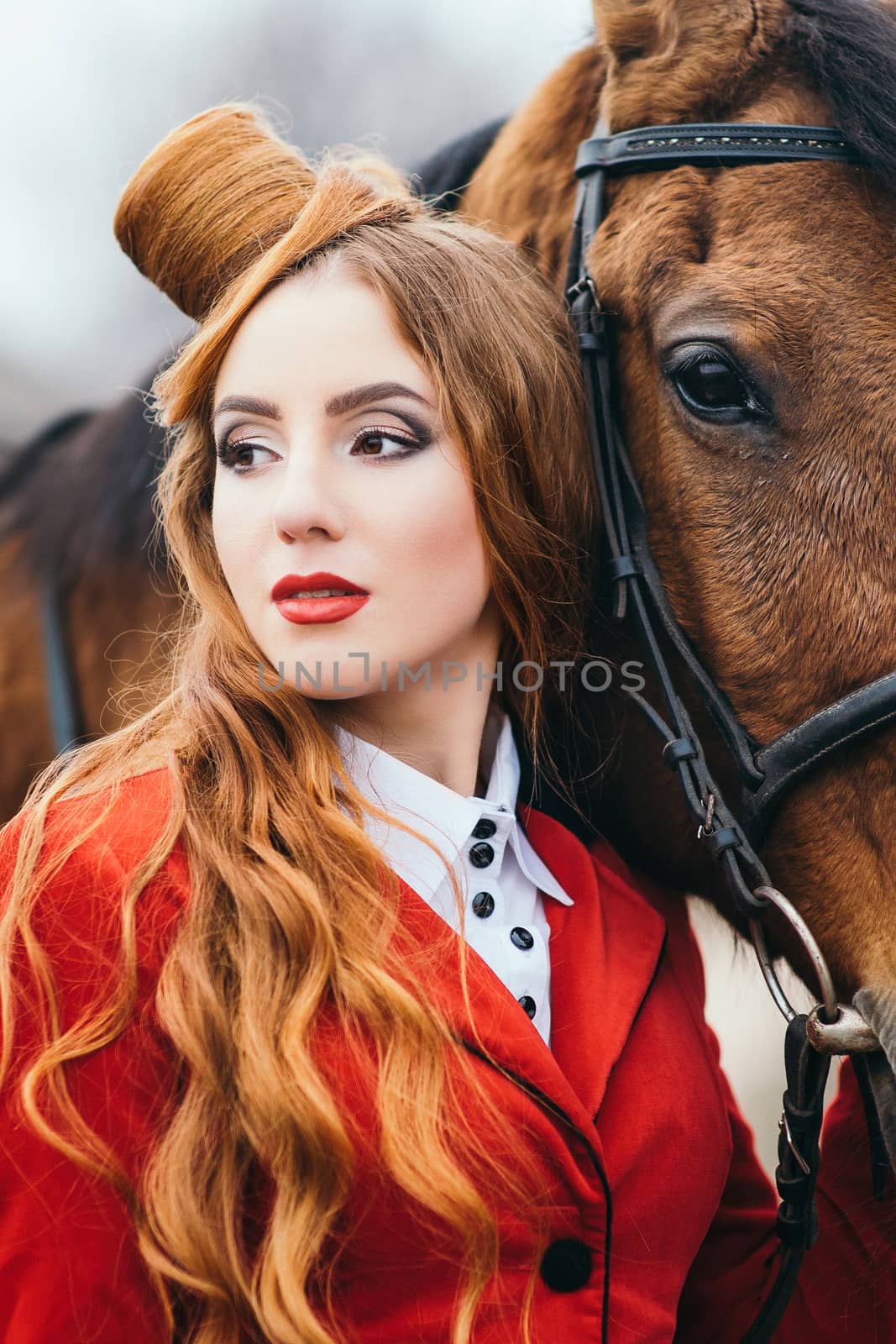 red-haired jockey girl in a red cardigan and black high boots with a horse for a walk