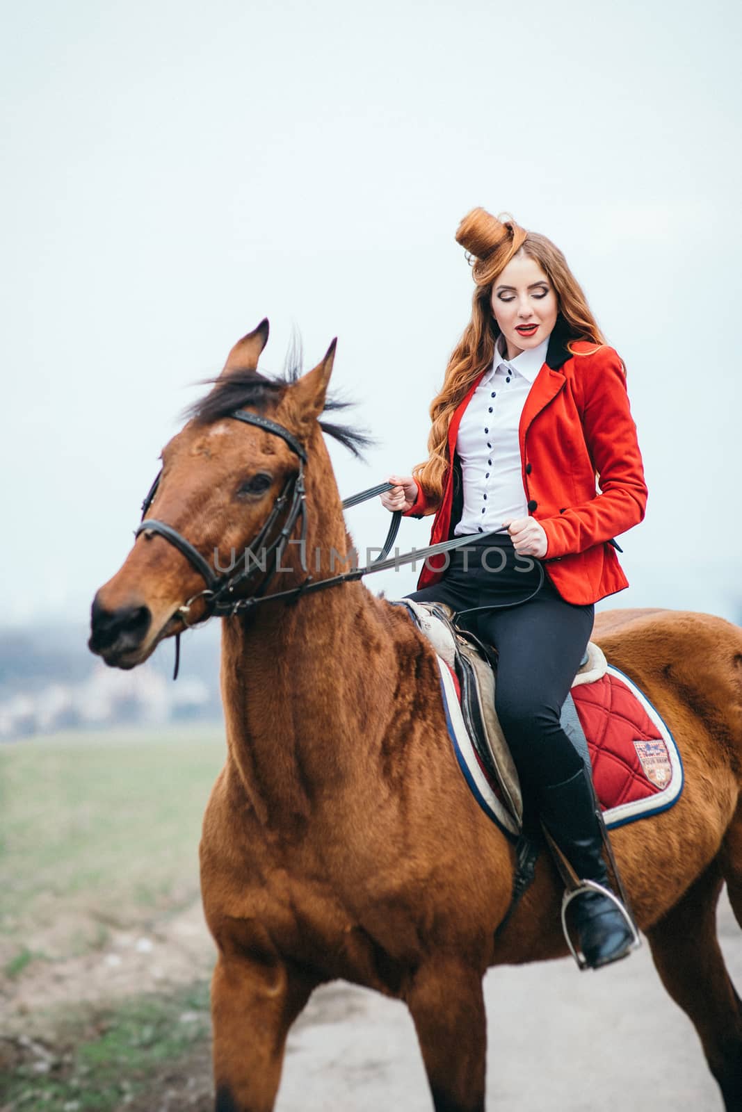 red-haired jockey girl in a red cardigan and black high boots with a horse for a walk