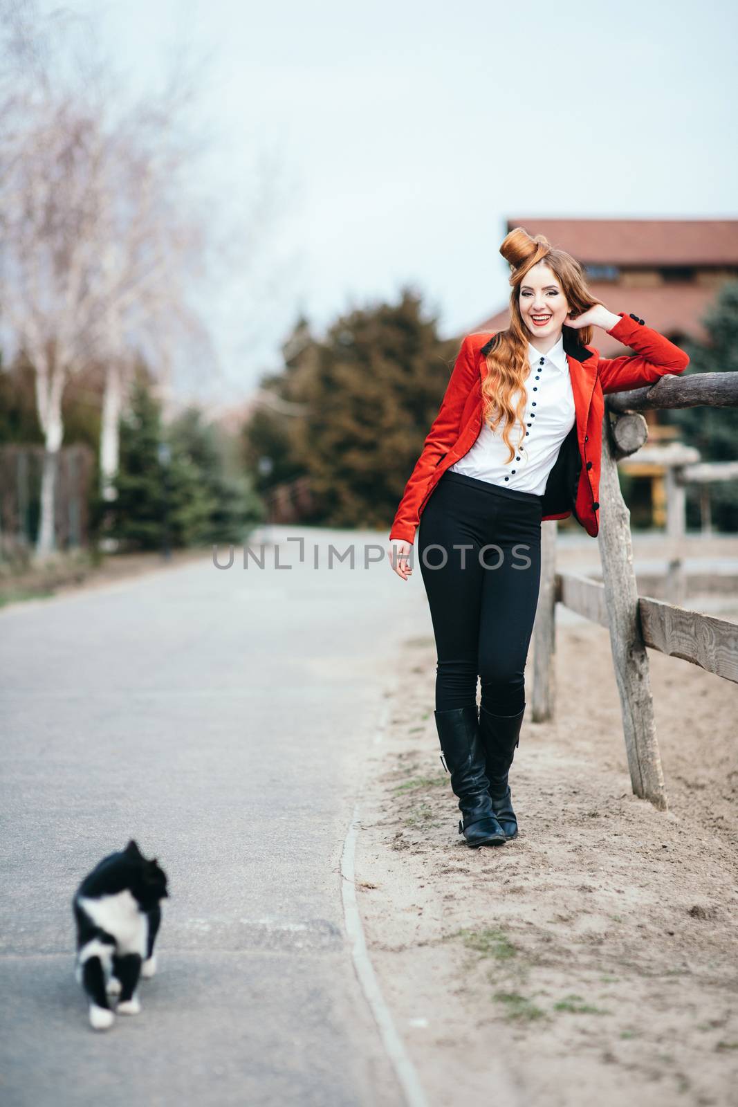 red-haired jockey girl in a red cardigan and black high boots with a cat for a walk