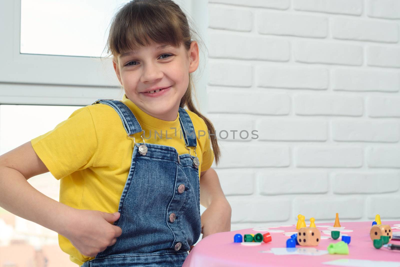A contented nine-year-old girl looked into the frame, sitting at the table and playing a board game