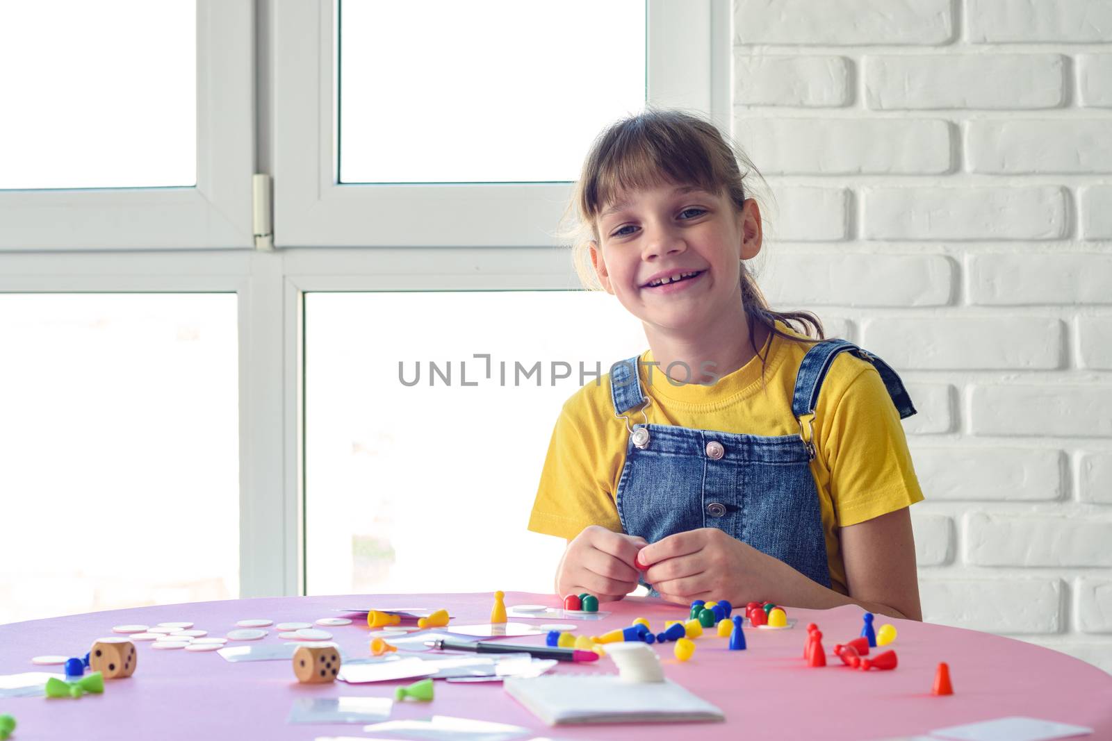 Cheerful girl plays board games at the table and looked into the frame
