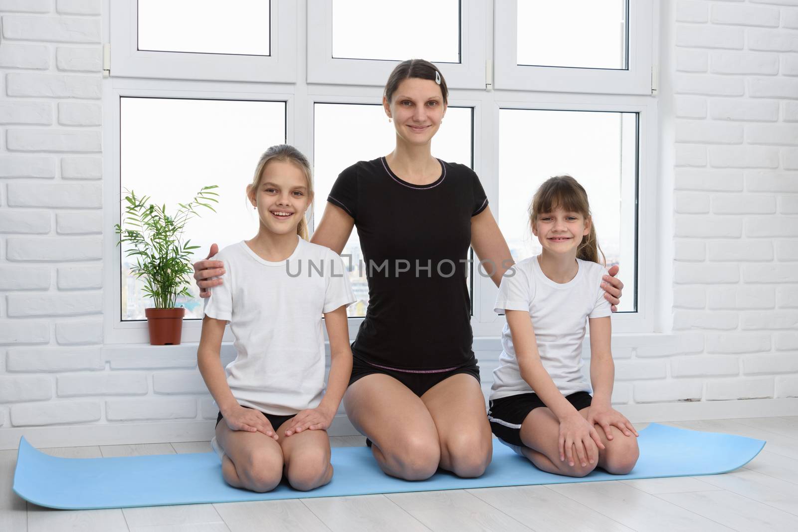 Mom and daughters in sportswear at home on fitness mat by Madhourse