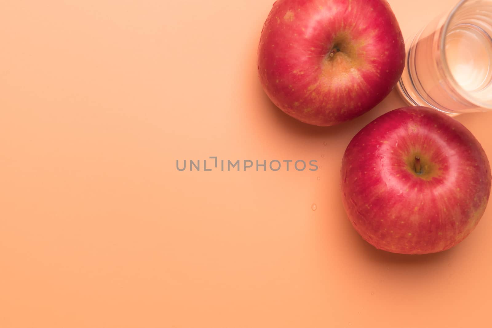 red apple and glass of water isolated on orange background, healthy food and fitness concept