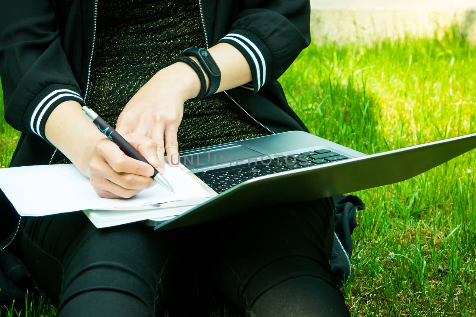 A young student woman is writing note while looking at laptop computer screen