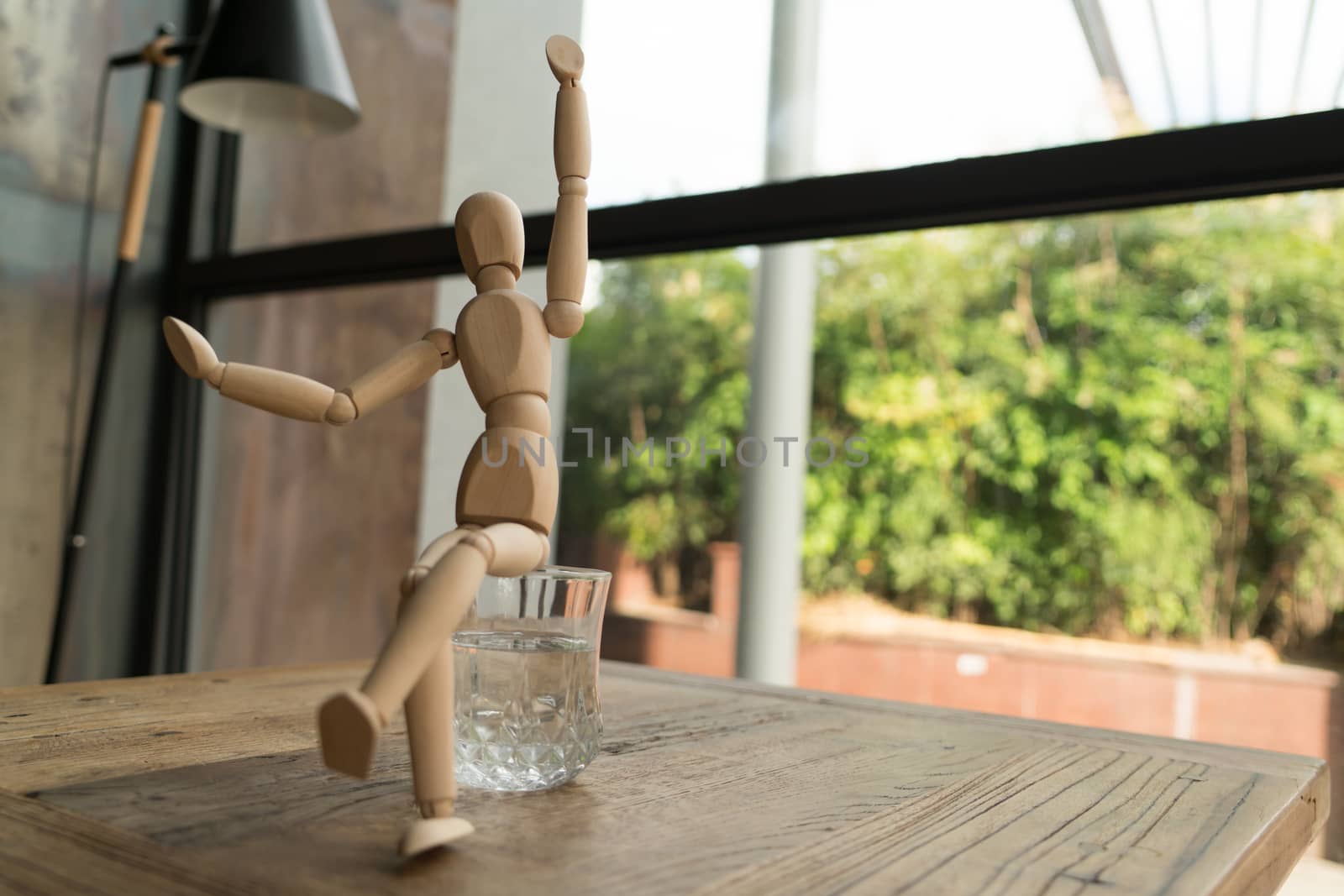 wood man is sitting on a glass of water while raise hand up