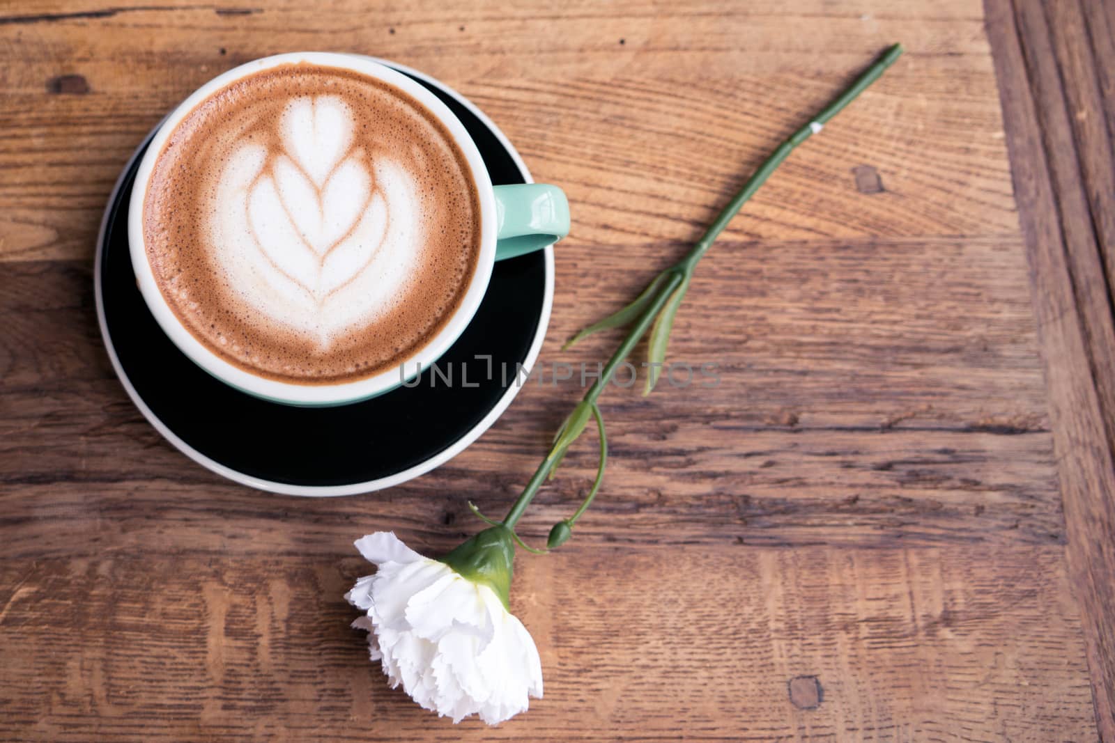 Hot mocha coffee or capuchino with heart pattern and white carnation flower on the wooden table