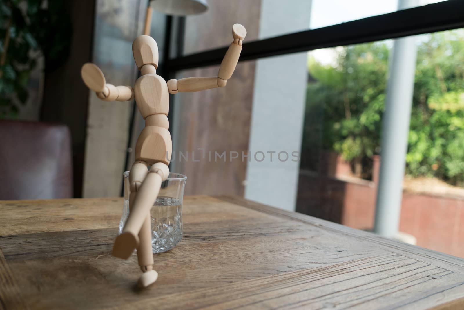 wood man is sitting on a glass of water while raise hand up