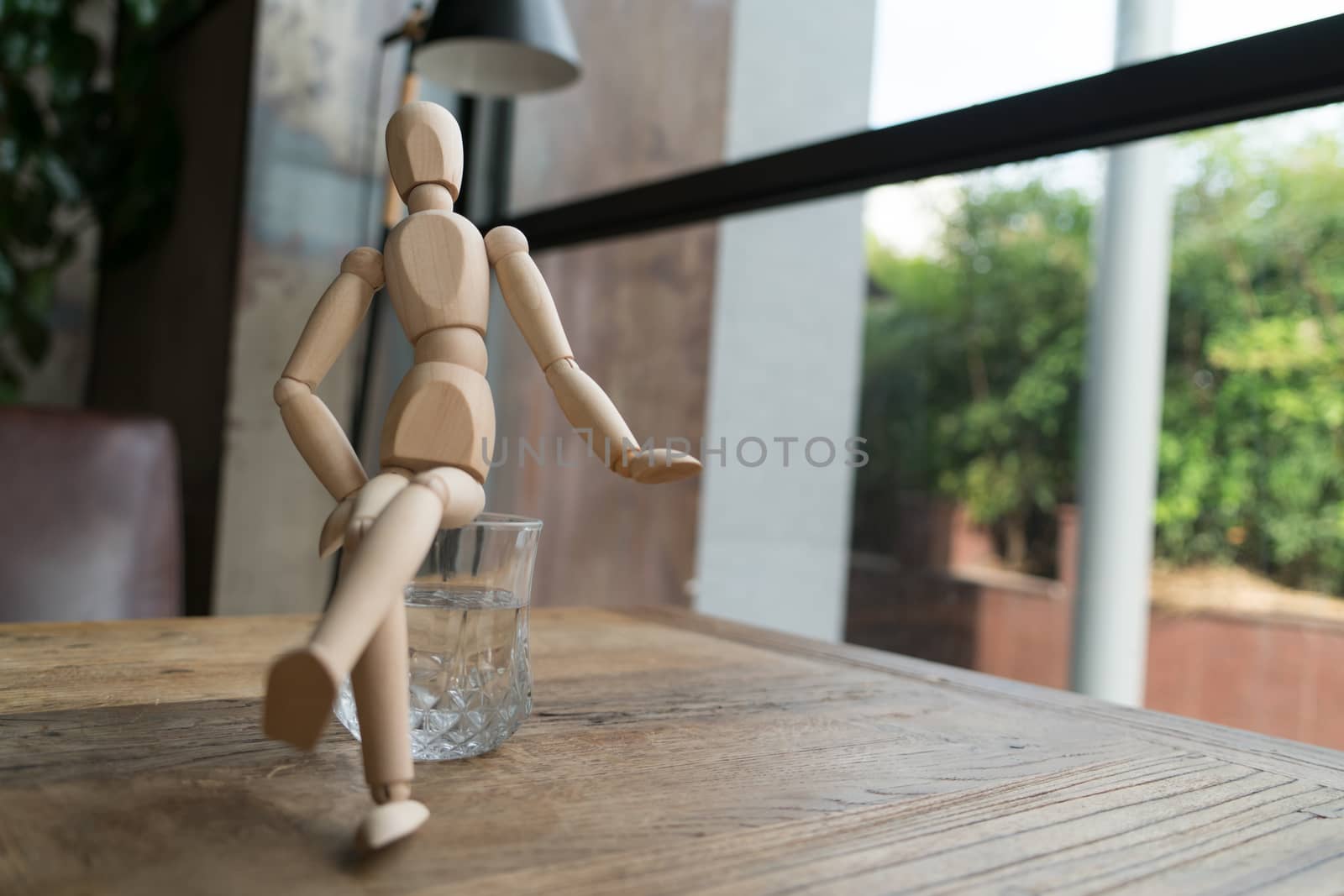 wood man is sitting cross-leg on a glass of water