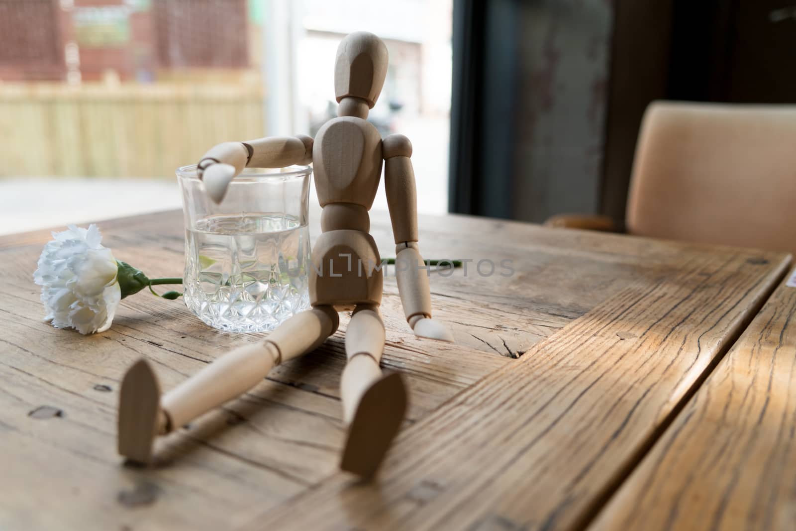 a wood man is sitting and put the arm on the glass of water by psodaz